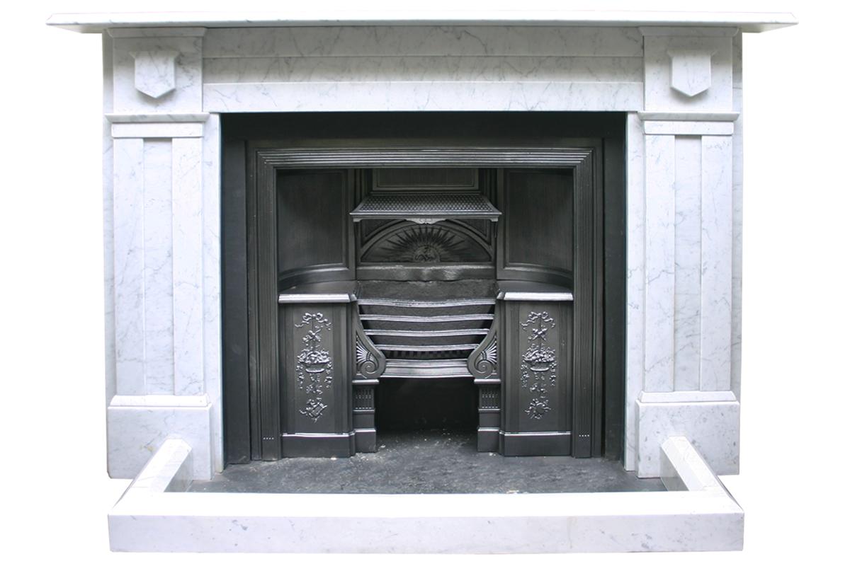 Antique early Victorian Carrara marble fireplace surround with recessed panel legs and carved shield capitals. Circa 1840.

For detailed sizes please see the size diagram in the image gallery.

Pictured with an original cast iron grate (now sold)