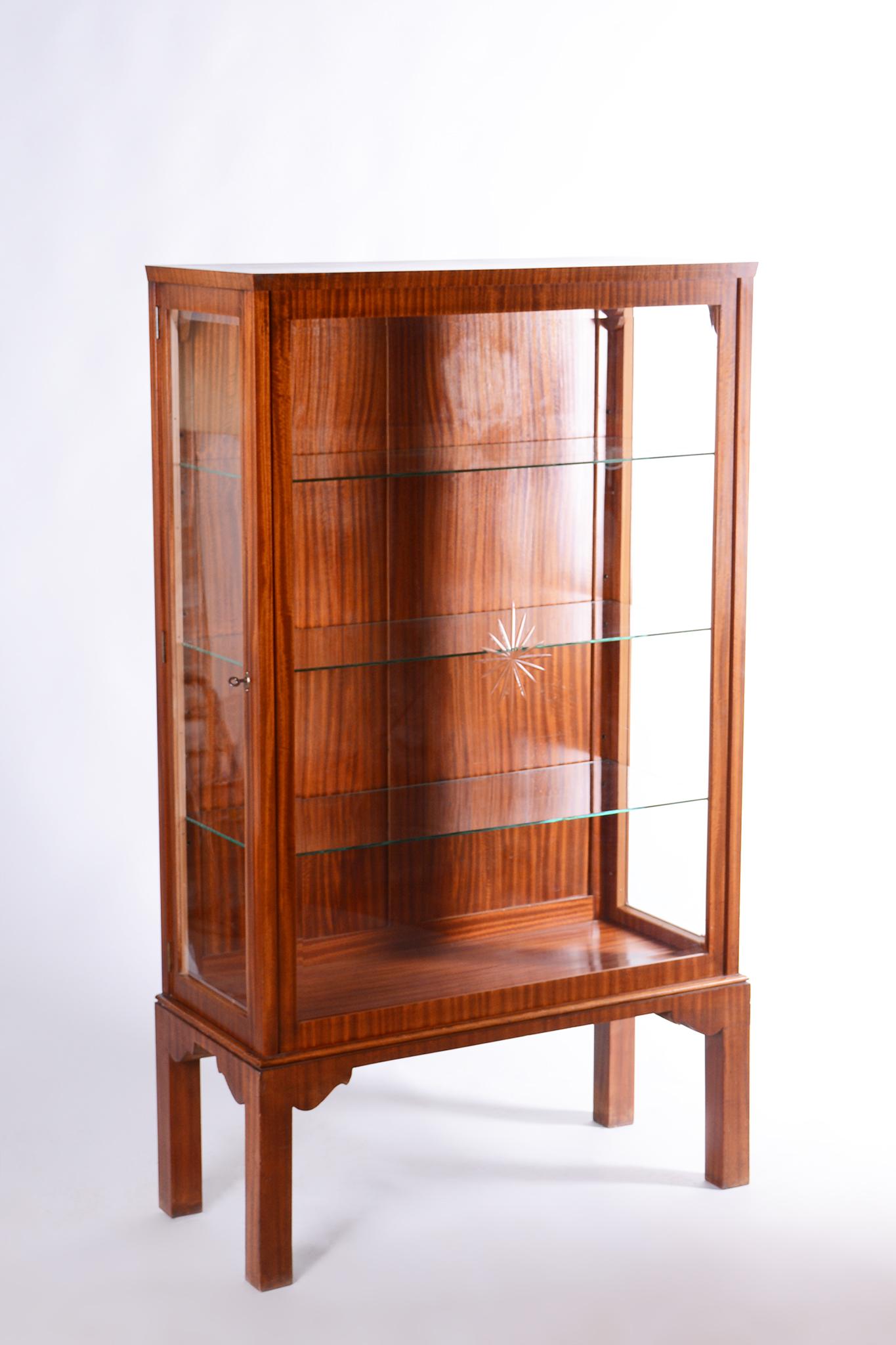 Esta elegante vitrina Art Déco data de la primera mitad del siglo XX. Está chapado en caoba y presenta paneles de cristal tallado transparente. Una característica práctica es la puerta lateral. El mueble se ha conservado en muy buen estado original,