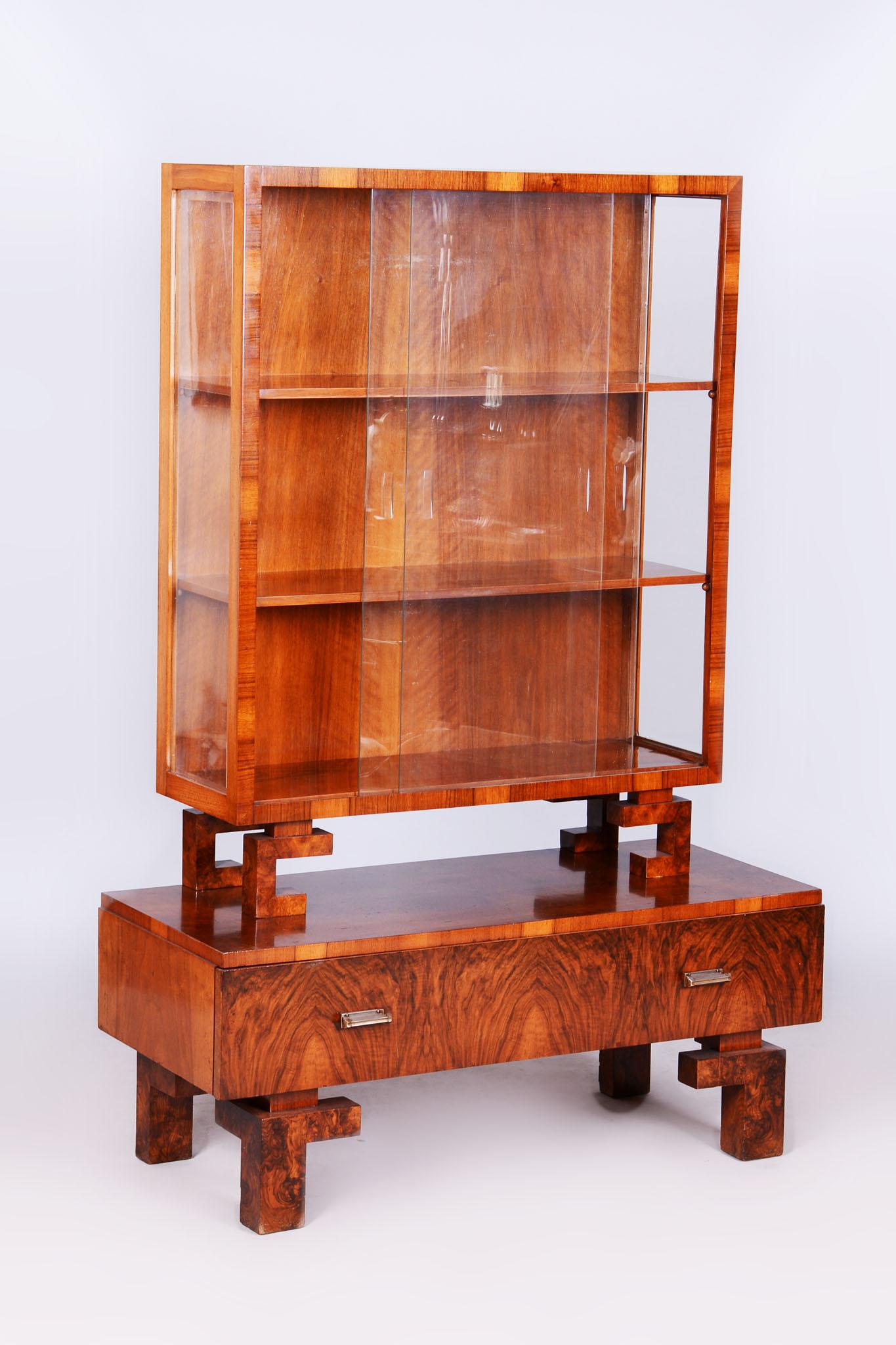 Questa elegante vetrinetta Art Déco dei primi del Novecento mette in mostra la maestria artigianale del design cecoslovacco. Realizzato in legno massiccio e impreziosito da un'impiallacciatura in noce di alta qualità, emana un fascino lussuoso e