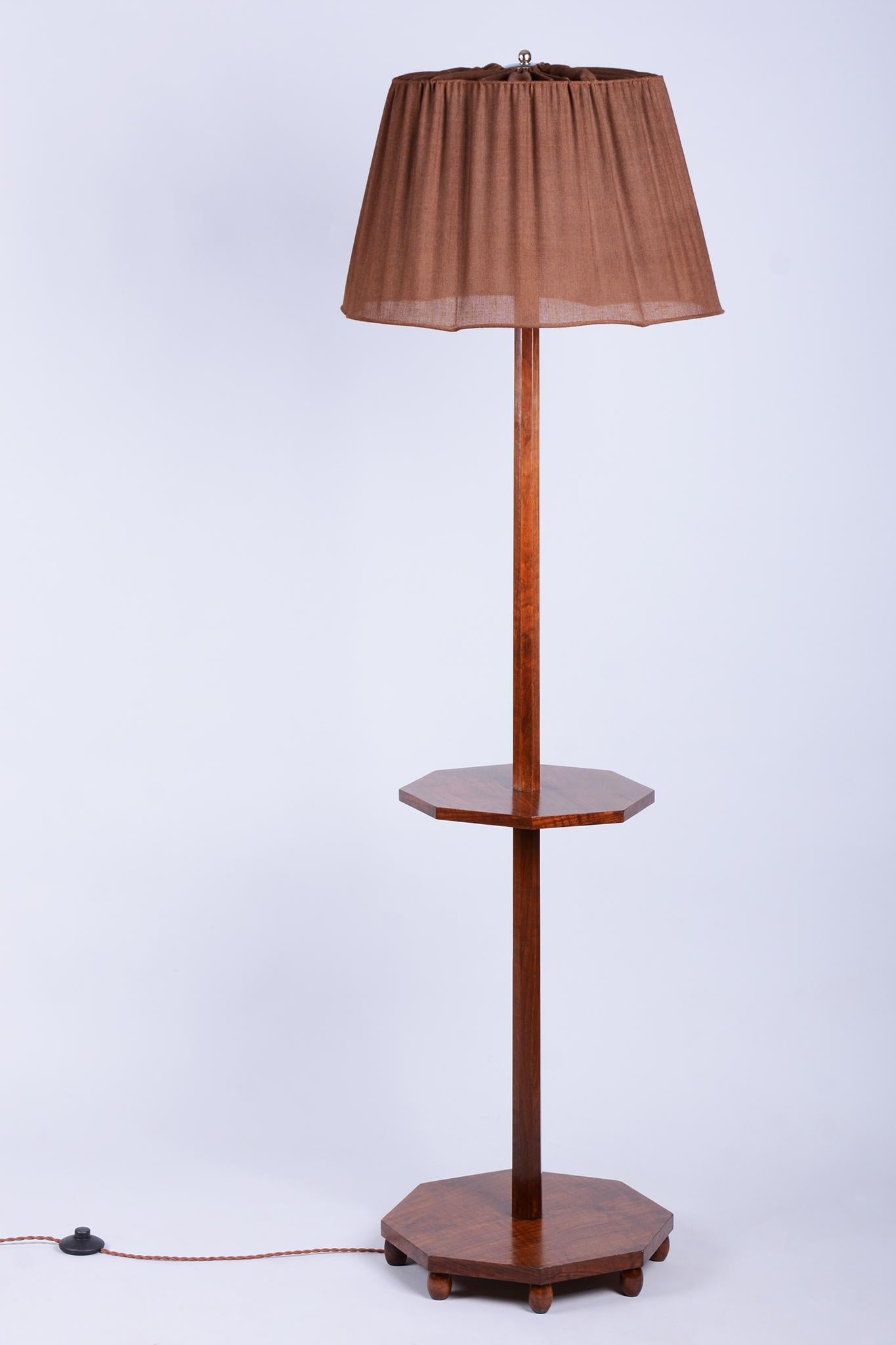 This elegant Art Deco floor lamp originates from Czechoslovakia from the 1920s. It is crafted from solid walnut and walnut veneer, which gives it a rich and timeless appearance with beautiful wood grain.

The lamp has undergone meticulous