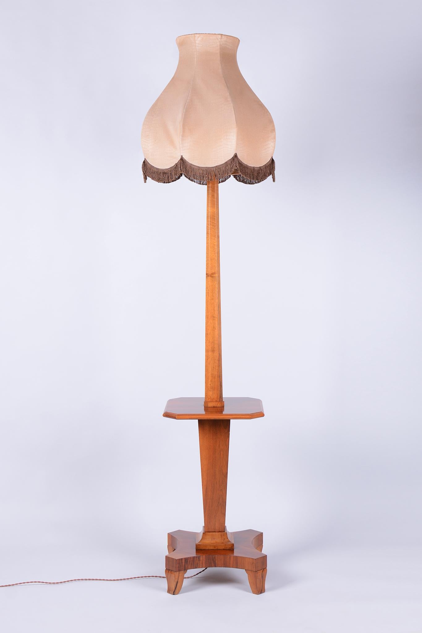 This elegant Art Deco floor lamp originates from Czechoslovakia from the 1920s. It is crafted from solid walnut and walnut veneer, which gives it a rich and timeless appearance with beautiful wood grain.

The lamp has undergone meticulous