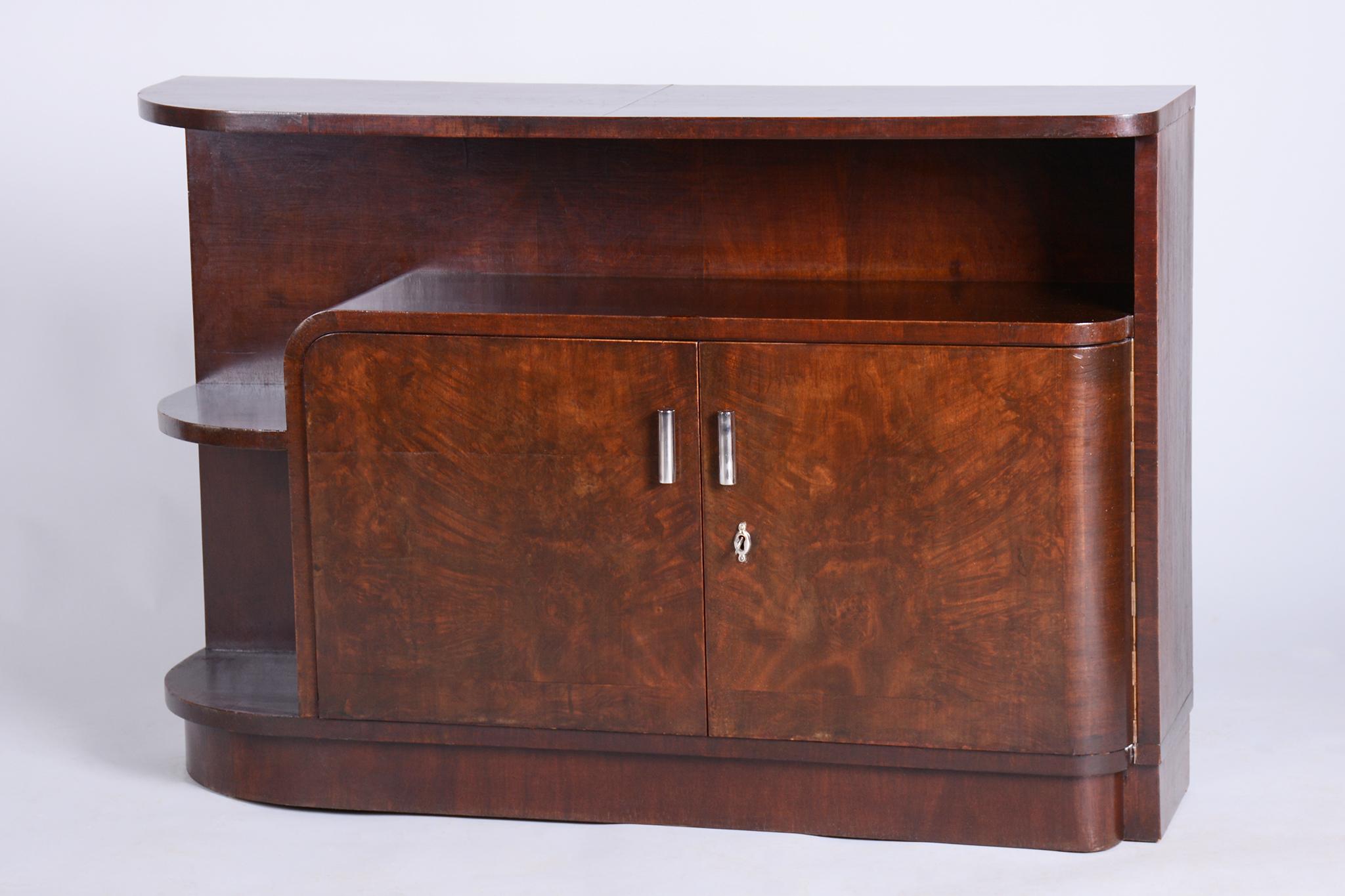 This elegant cabinet from the 1930s showcases an interesting fusion of Art Deco and Bauhaus elements. Originating from Czechoslovakia, it is crafted from high-quality blockboard veneered with walnut and walnut burr. Chrome steel handles emphasize
