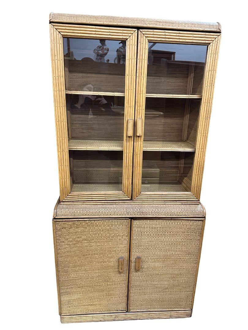 Immerse yourself in timeless elegance with our meticulously restored Art Deco Stick Rattan Bamboo Grass mat Glass China Cabinet/Etagere. The Etagere features a top breakfront with 2 glass doors and 3 fixed shelves and bottom cabinet with two doors
