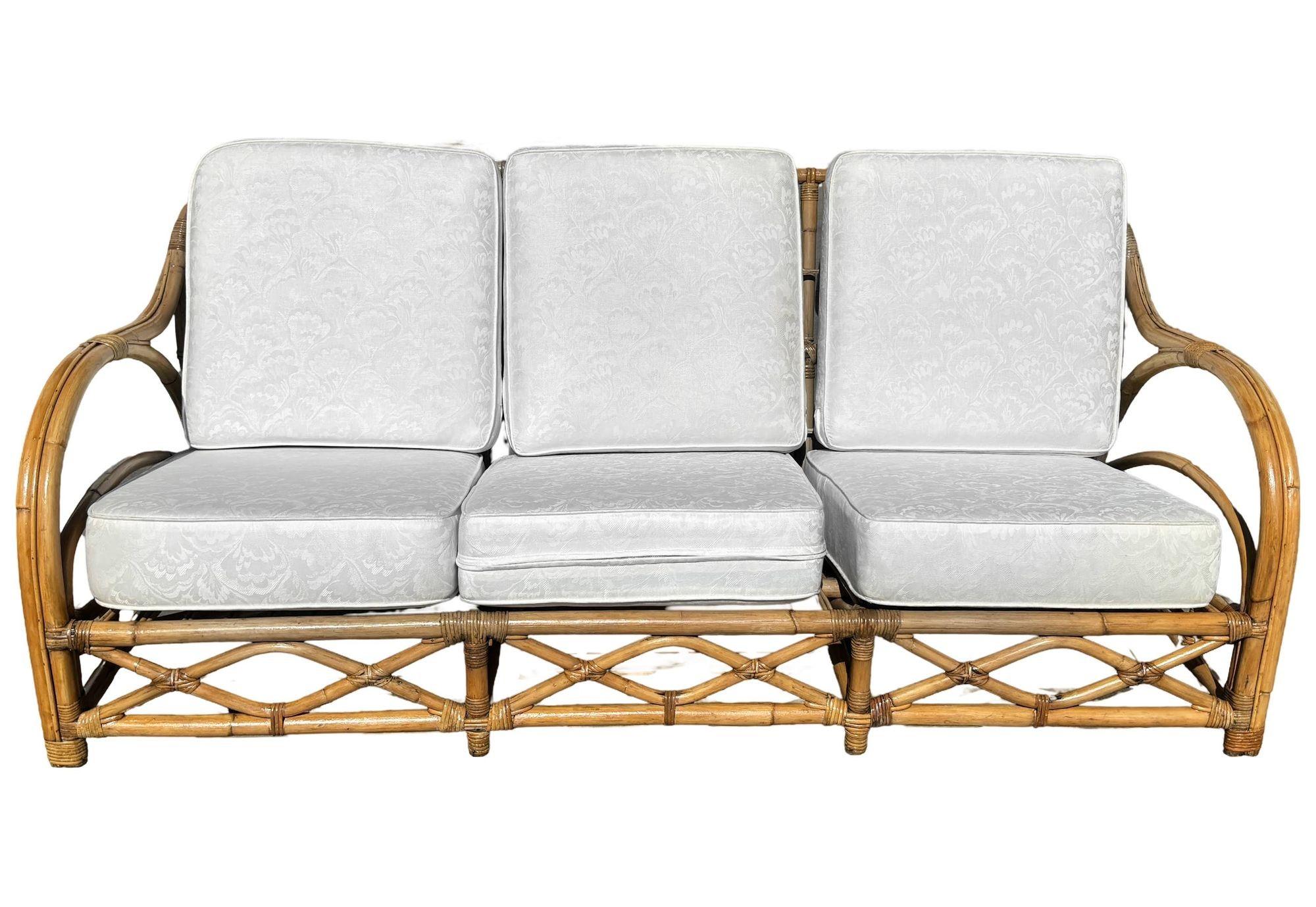 This beautifully restored Art Deco rattan three-seat sofa features the classic transitional arms with double-strand arms accented by a center stick strand in the center. The intricate lattice front, stick rattan back, and corner wrappings make it a