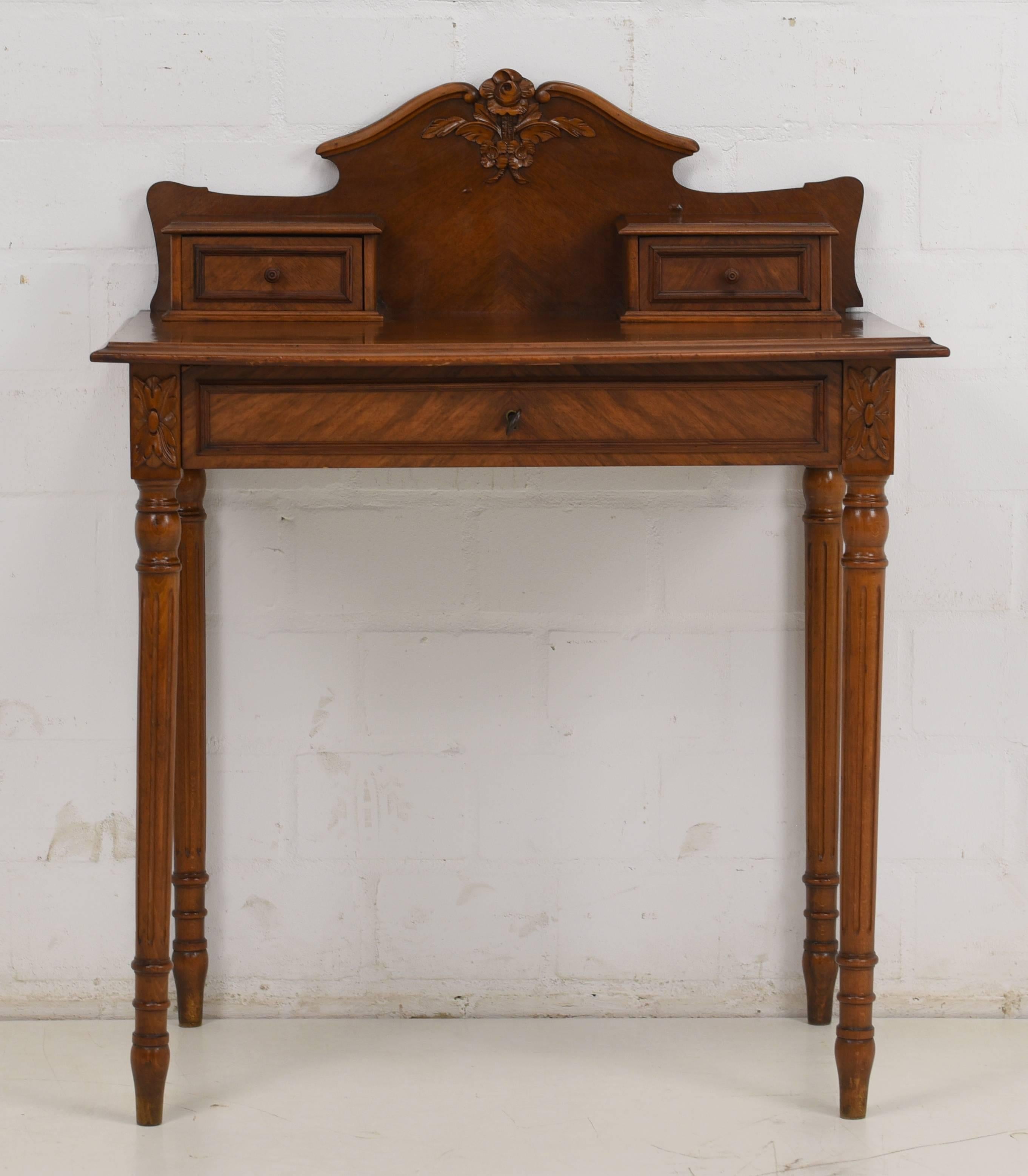 An Art Nouveau ladies desk from circa 1920. It has a wonderful walnut wood veneer with a squared veneer on the plate. Above the plate are two smaller drawers and below a bigger one which is lockable. Beautiful carving decor is at the back of the