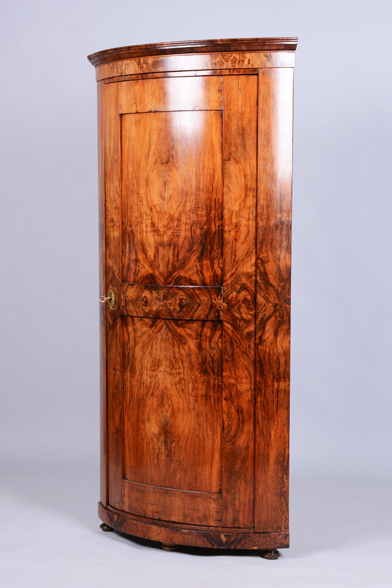 This unique Biedermeier corner cabinet originates from Austria from the first half of the 19th century. It is crafted from solid spruce wood and veneered with walnut, which boasts an unusually rich and distinctive wood grain. Every detail of the