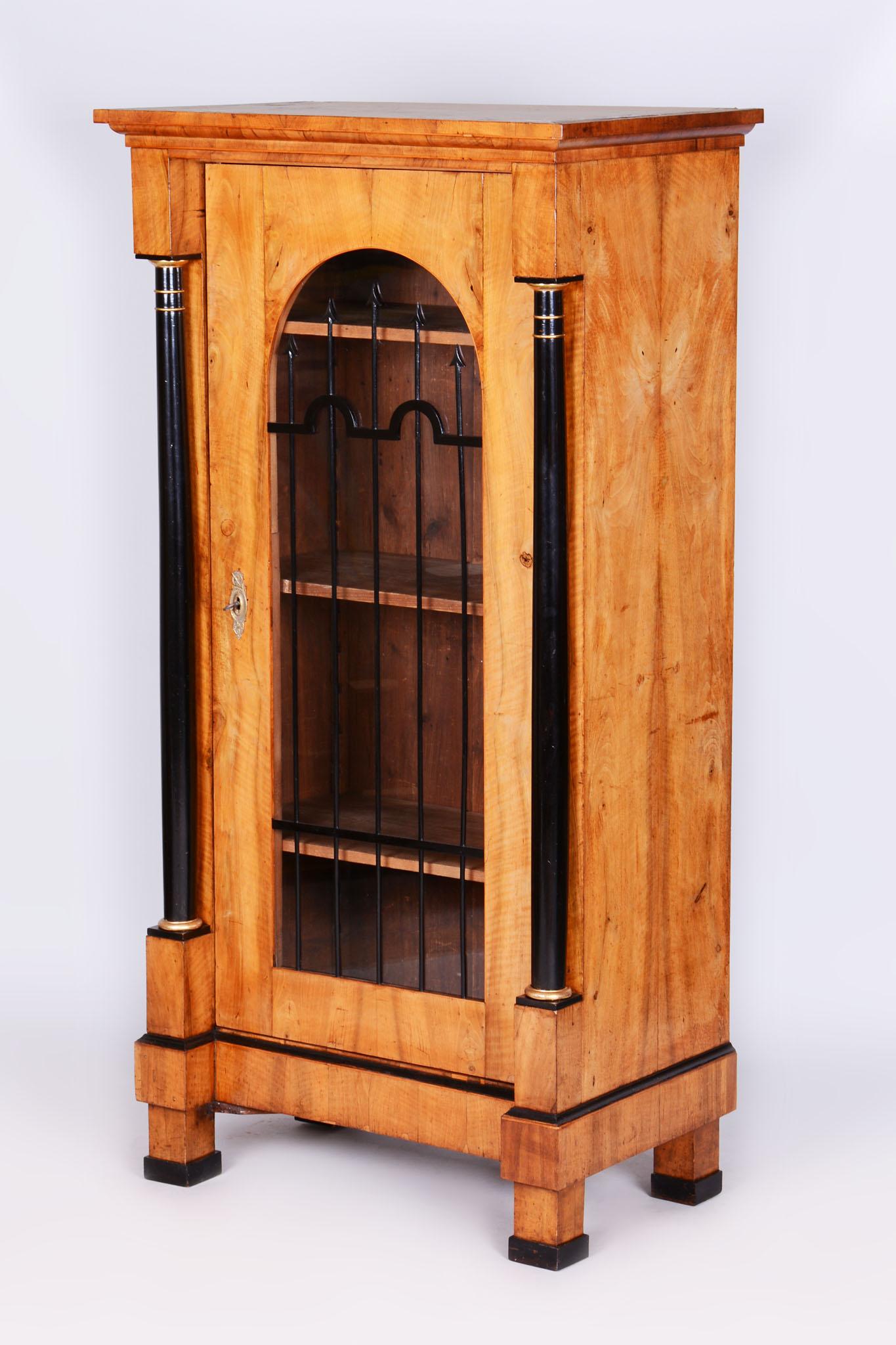 Esta impresionante vitrina, de estilo Biedermeier, data de principios del siglo XIX y se fabricó en Austria. Está construido con madera de nogal fino y adornado con detalles ebonizados y dorados que realzan su aspecto elegante. Restaurada por