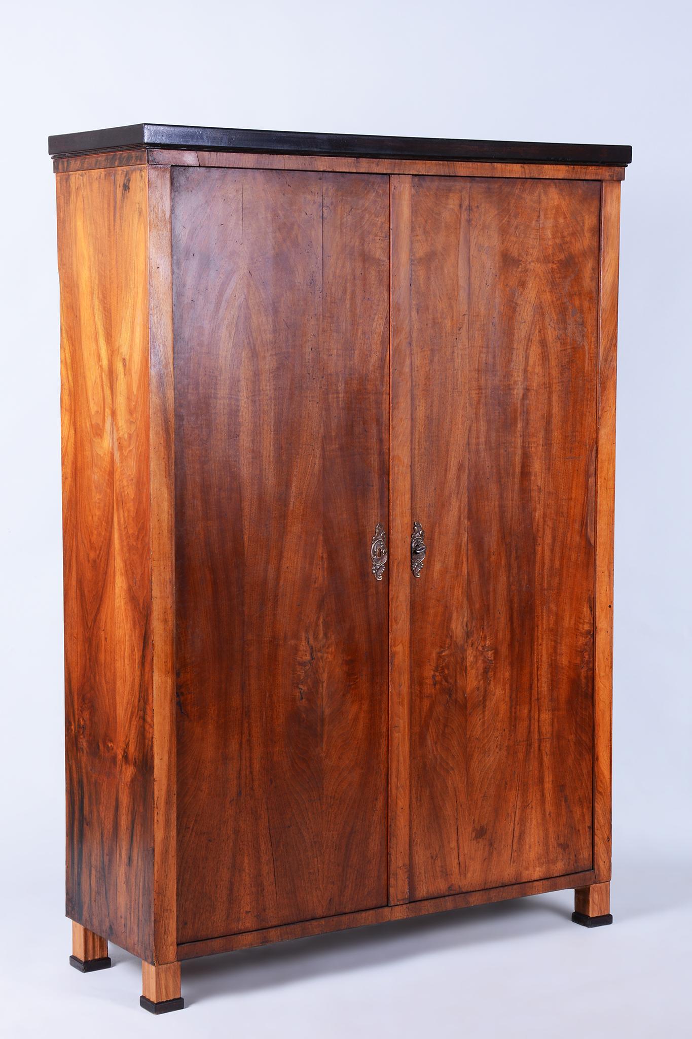 Cette authentique armoire à deux portes Biedermeier est originaire de Bohemia, au début du 19e siècle. Sa carcasse est fabriquée en bois d'épicéa massif plaqué de noyer, ce qui lui confère un aspect classique et intemporel avec de belles veines de
