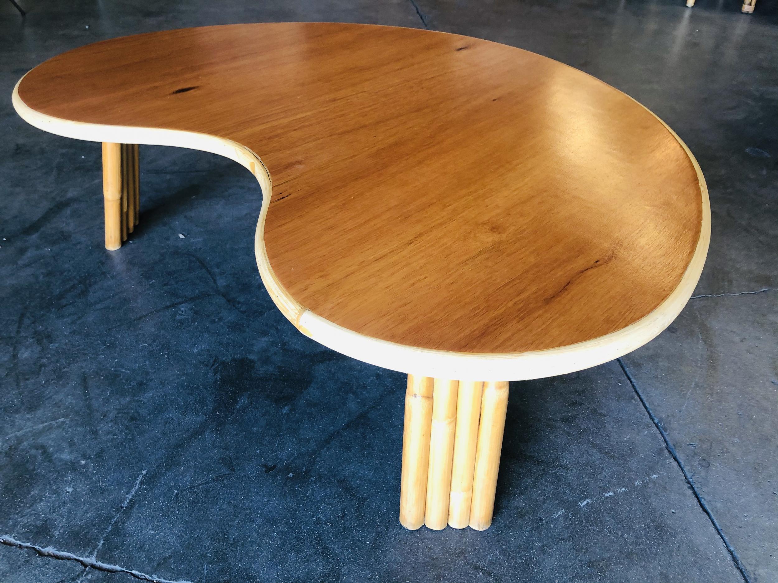 Biomorphic coffee table with vertically stacked rattan legs and a mahogany wood top with a rattan trim along the borders. 

Restored to new for you.

All rattan, bamboo and wicker furniture has been painstakingly refurbished to the highest standards