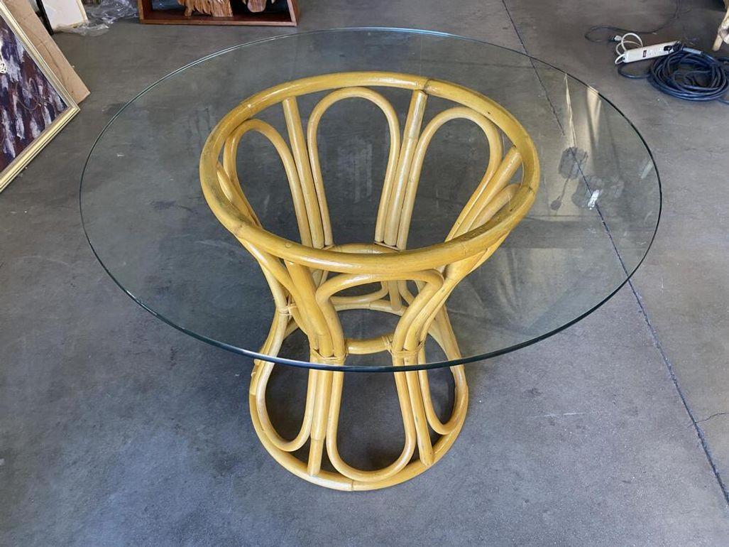 Elegant midcentury dining table features a sculptural hourglass rattan base with a round glass top. The table can easily accommodate four guests depending on the choice of chairs. The Diameter of a glass top would be 24