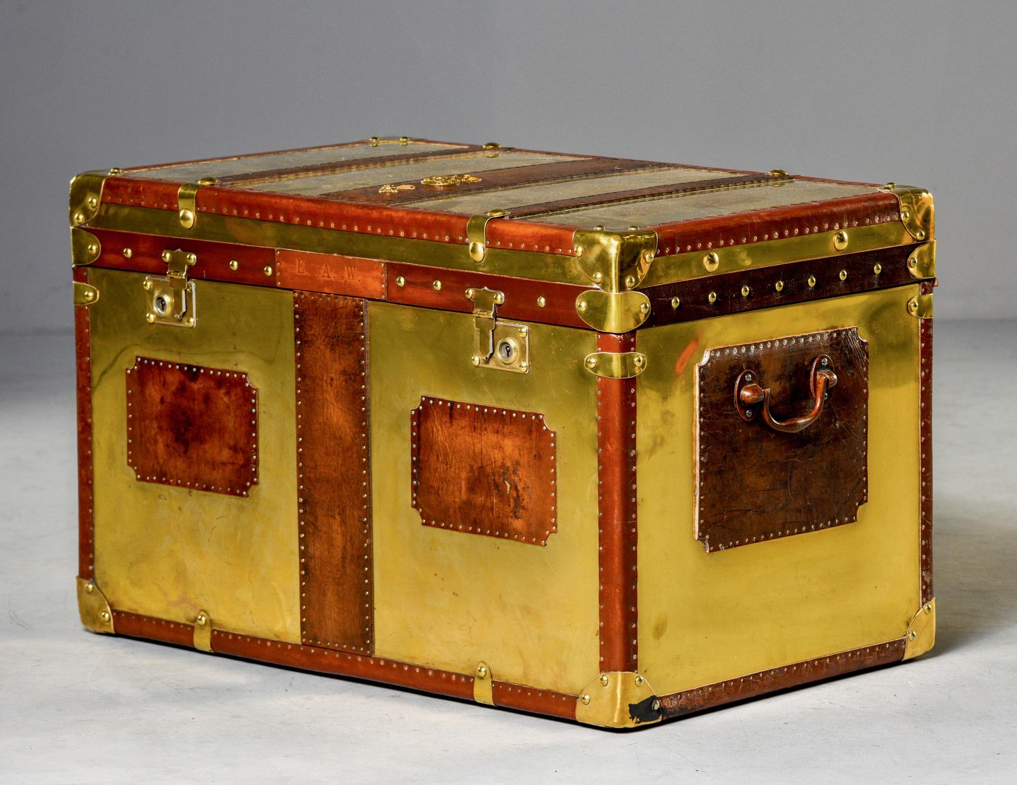 English brass and leather trunk with hinged lid circa 1930s. Wooden trunk is covered in weathered leather and polished brass and English grenadier’s ornamental details. New royal blue fabric lining and restored leather interior. Unknown maker.