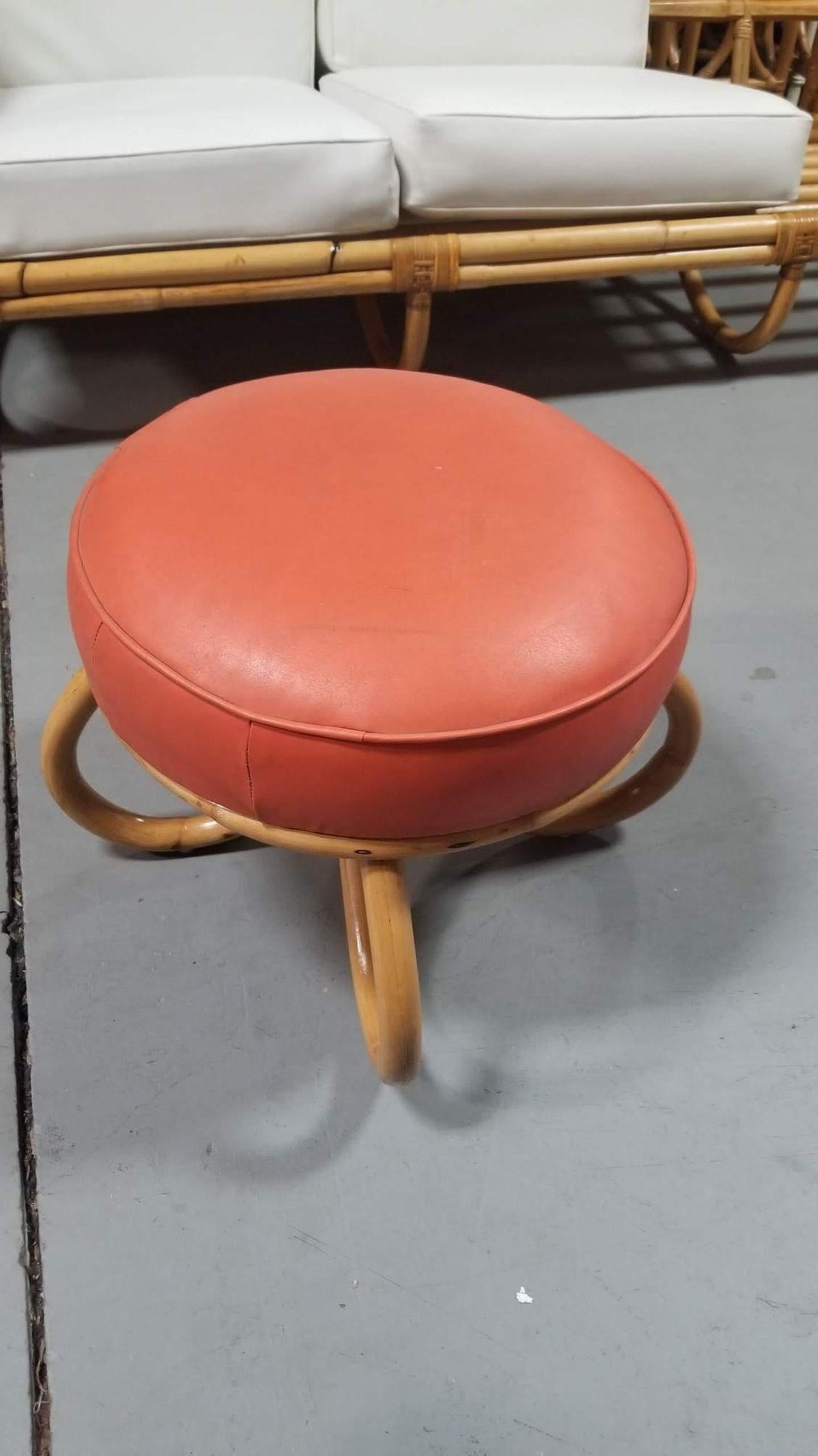 The Restored Coral Orange Naugahyde Footstool, adorned with vibrant Naugahyde upholstery and rattan loop legs, harmonizes vintage allure and modern sophistication. Its retro charm is revitalized through the bold coral orange hue, while the intricate