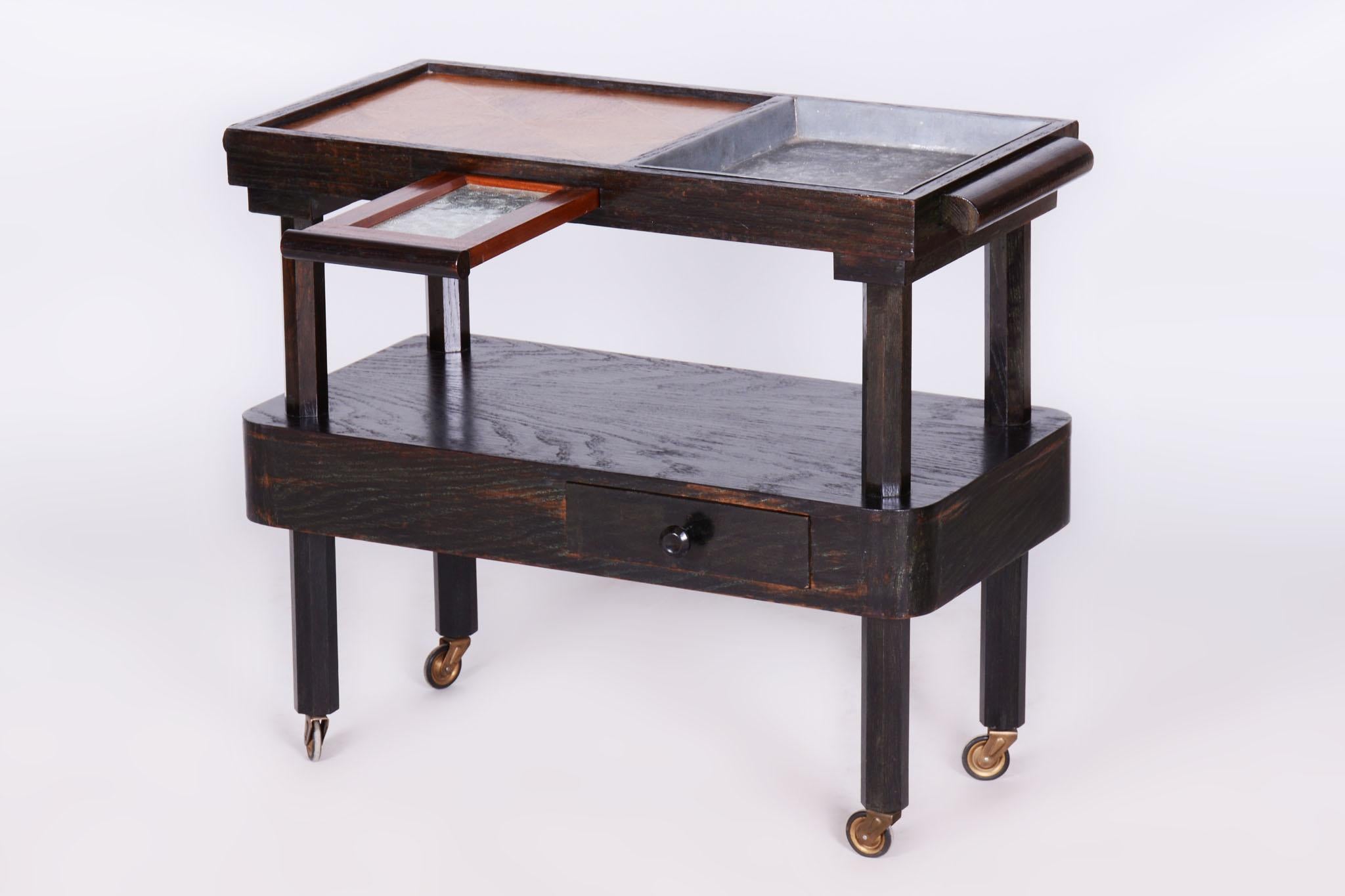 Questo elegante tavolo da portata cubista proviene da Bohemia e risale agli inizi del XX secolo. È realizzato in rovere massiccio, impiallacciato in rovere, intarsi in mogano, vetro e metallo galvanizzato.

Il tavolo è stato sottoposto a un accurato