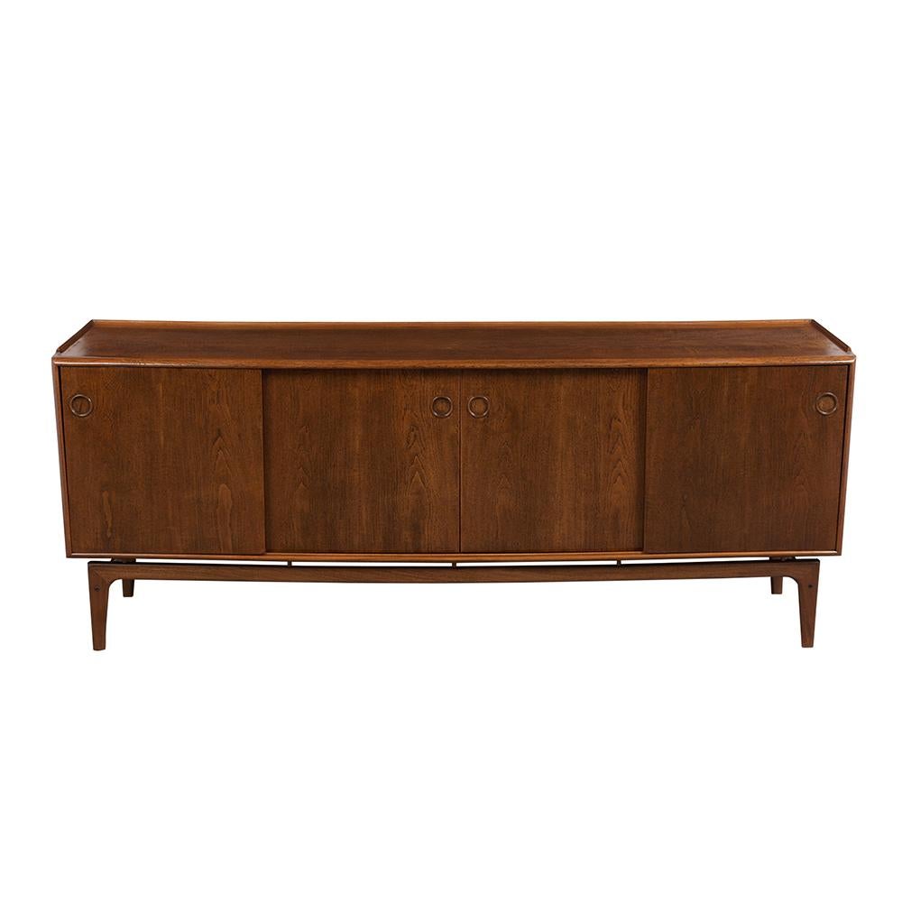 This Danish modern style credenza has been completely restored and stained in walnut color with a lacquered finish. It features four large sliding doors with unique circular carved wood inserts handles. The right side of the credenza has three small