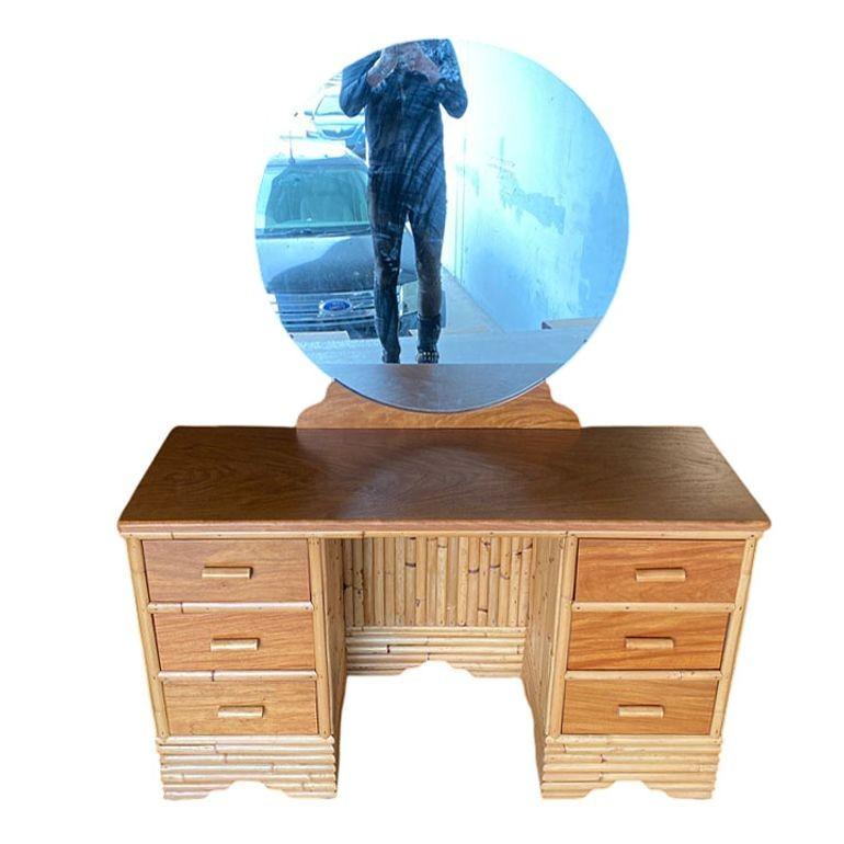 This beautifully restored Paul Frankl-inspired rattan vertically staked rattan vanity blends style vintage charm with modern comfort. It features a Filipino mahogany table top, drawer fronts, and a round mirror. The vanity features a cut-out for