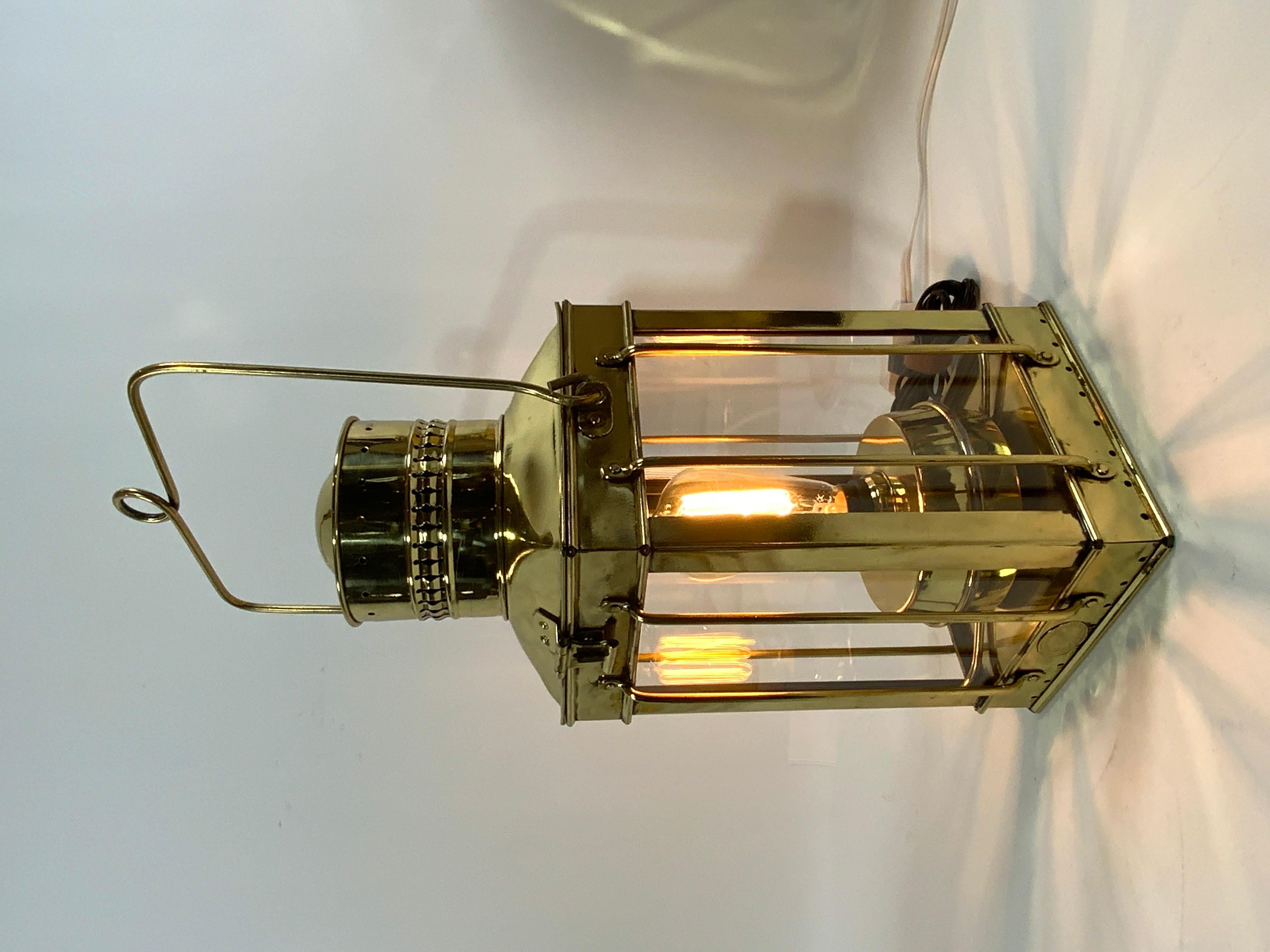 Highly polished and lacquered English ships lantern of brass. Meticulously polished and lacquered. Oil tank has been retrofitted with a led bulb and wire. Four glass panes and protective brass bars. Vented chimney. Hoisting handle Circa 1920. In the