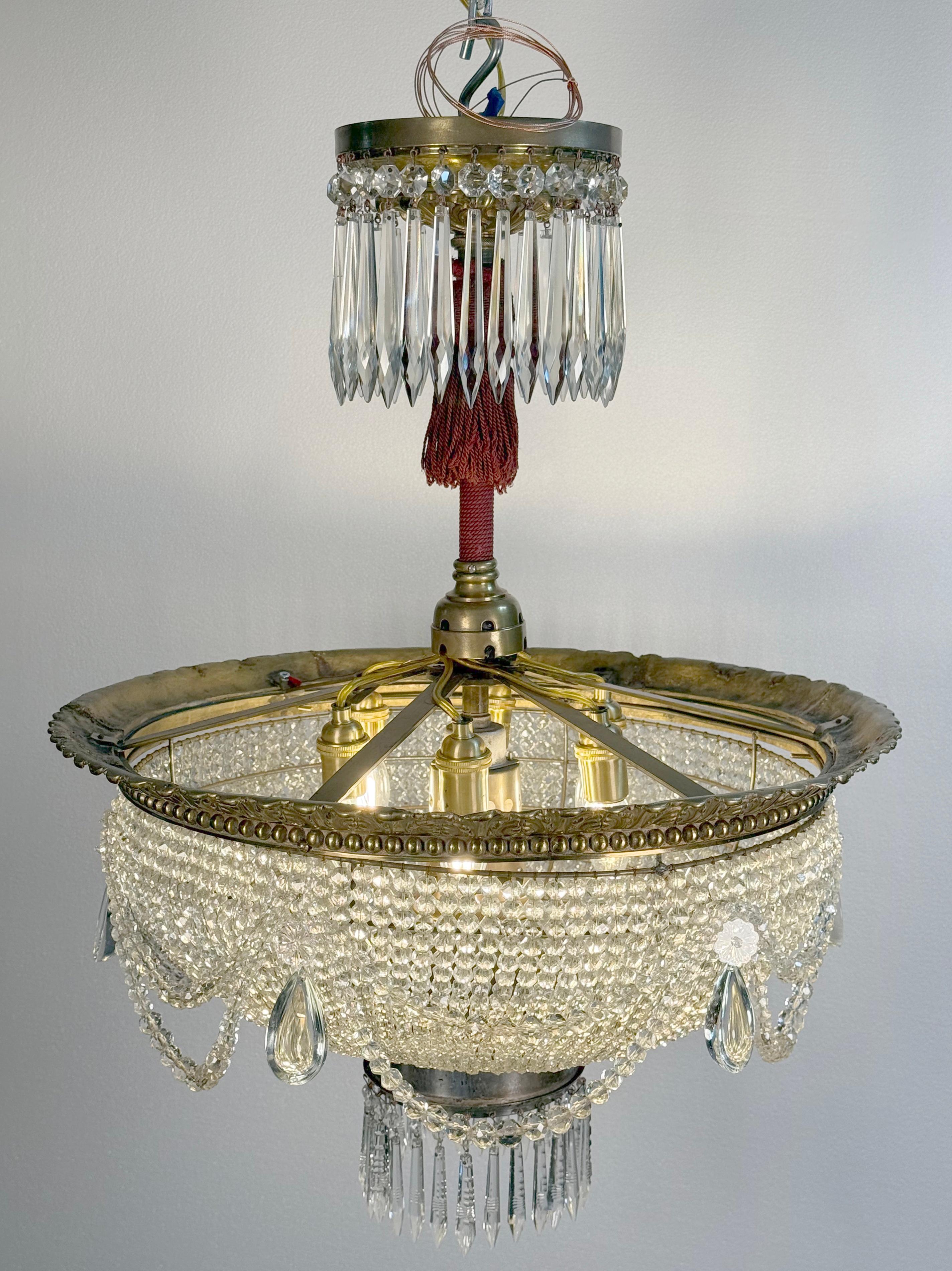 Lampadario a cestello in stile francese con cristalli sfaccettati a forma di ottagono drappeggiati, accentati da cristalli a forma di lancia sulla parte superiore e inferiore. C'è una nappina rossa intrecciata sul palo centrale. Telaio in ottone.