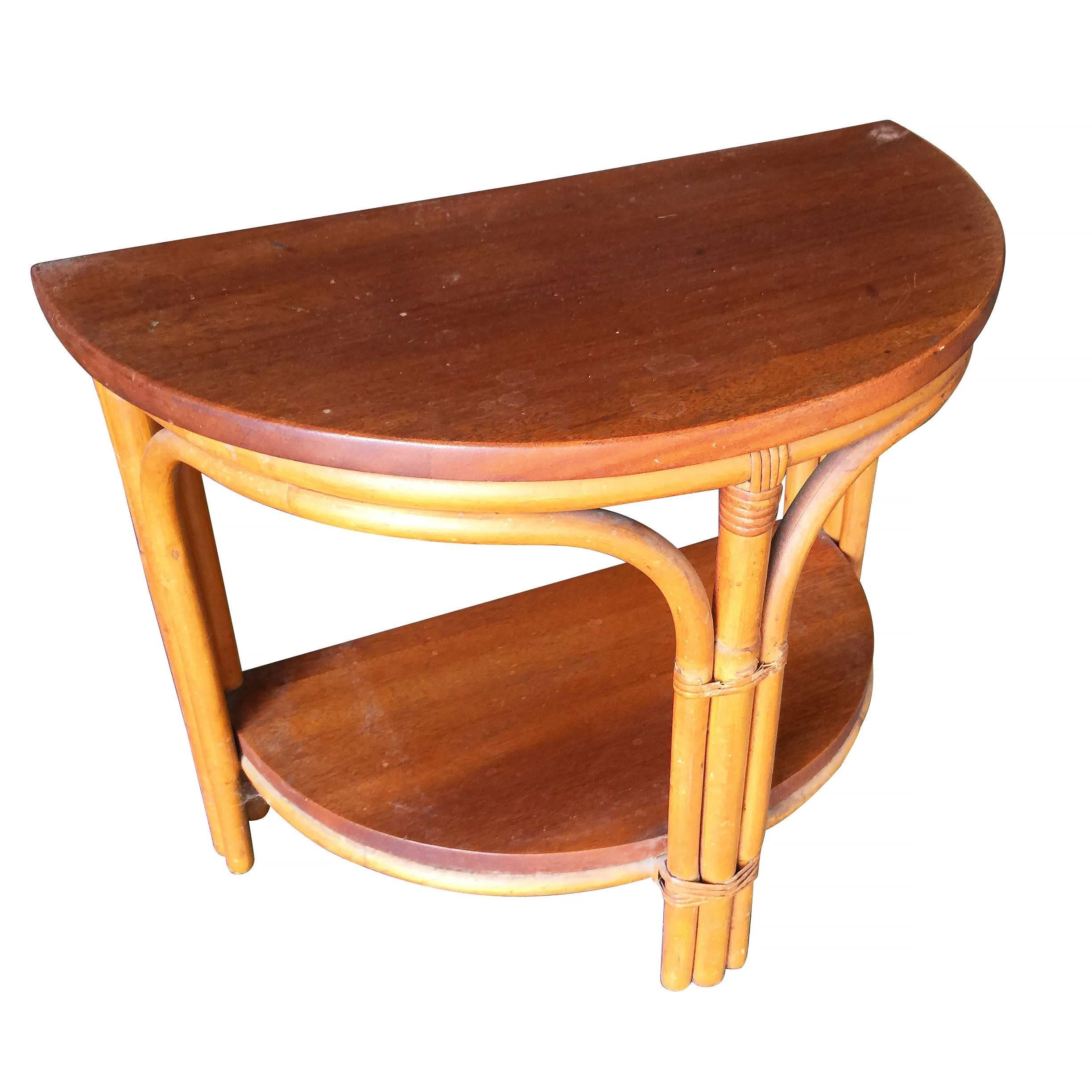 Vintage 1940s two-tier rattan side table featuring stylized three strand legs and beautiful half round mahogany tops. Pair Available

Restored to new for you.

All rattan, bamboo and wicker furniture has been painstakingly refurbished to the highest