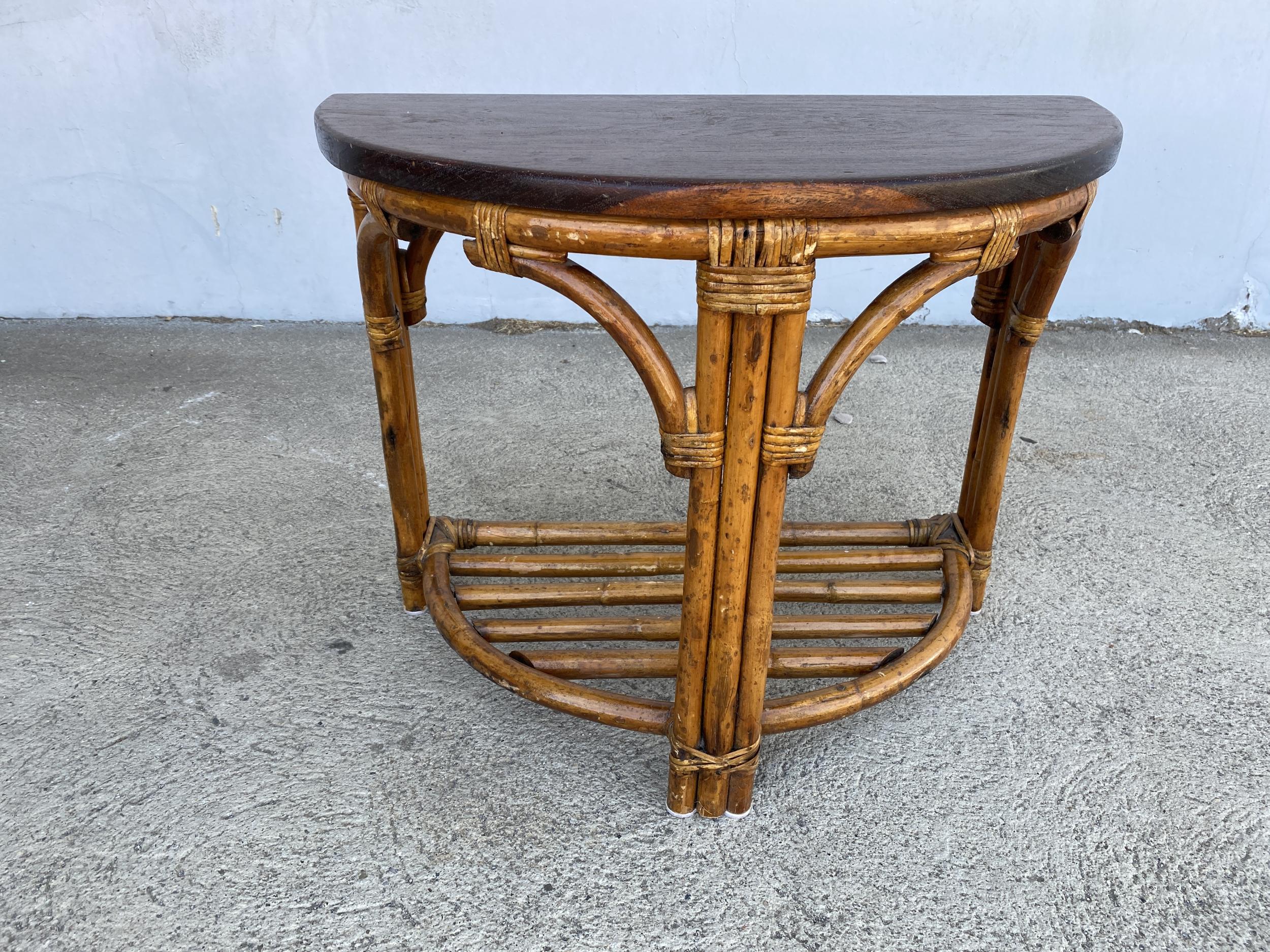 Vintage 1940s two-tier rattan side table featuring stylized three strand legs and beautiful half round mahogany tops. Pair Available

Restored to new for you.

All rattan, bamboo and wicker furniture has been painstakingly refurbished to the