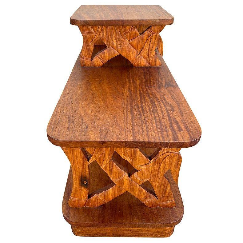 This beautifully restored 3-tiered side table is crafted from hand-carved koa wood featuring 2 front panels sculpted into the shape of bamboo poles with leaves. Koa wood is known for its distinctive grain and rich natural tones. The table features