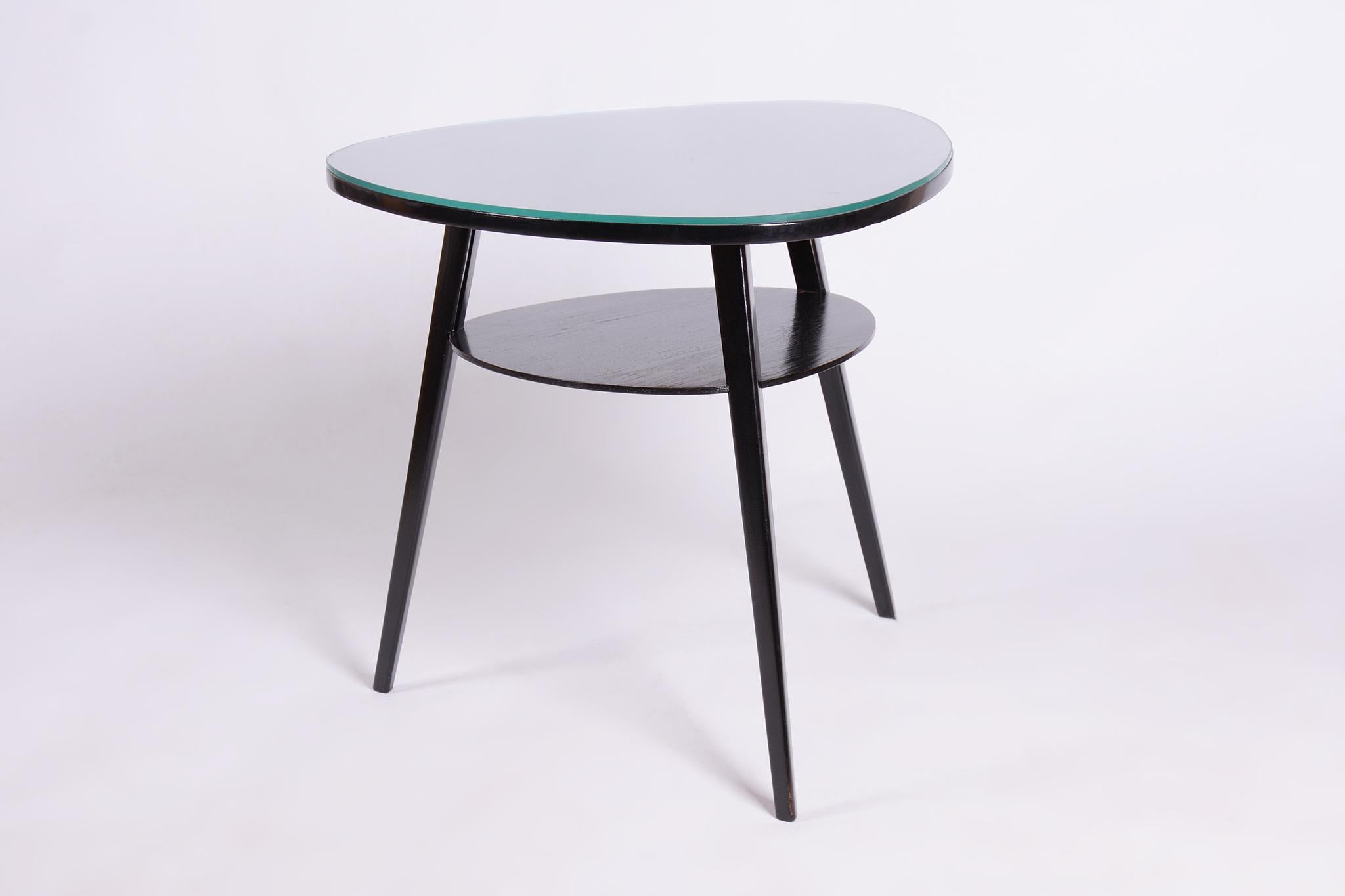 This elegant Mid-Century table comes from Czechoslovakia from the mid-20th century. It features beech legs and a tabletop made of oak blockboard, topped with a clear glass surface. The table has undergone careful restoration, has a stable