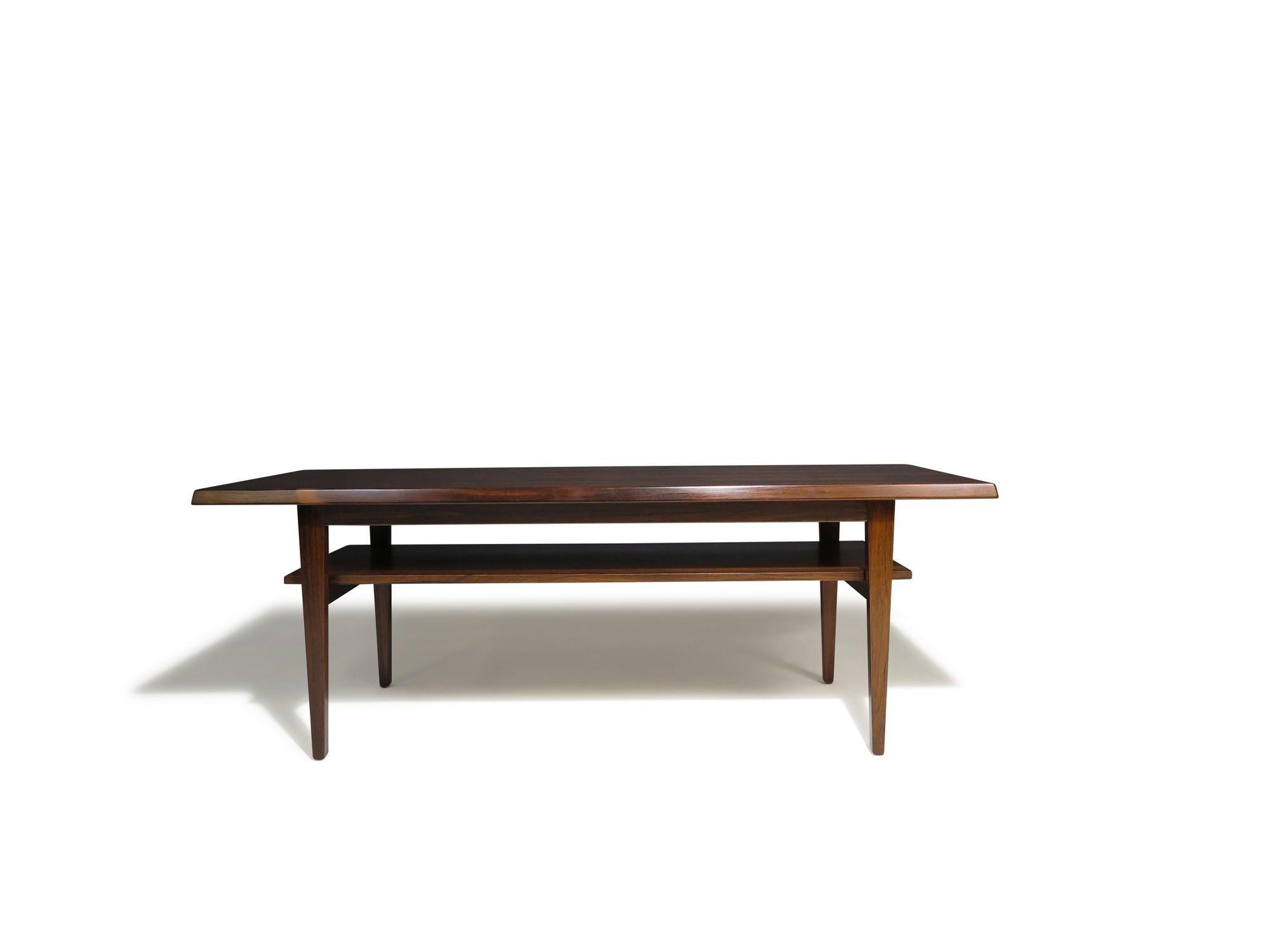 La table basse rectangulaire des années 1950 est fabriquée à partir d'un superbe palissandre brésilien assorti aux livres, présentant des motifs de grain dynamiques et de riches tons naturels. Le plateau de table présente des bords biseautés et