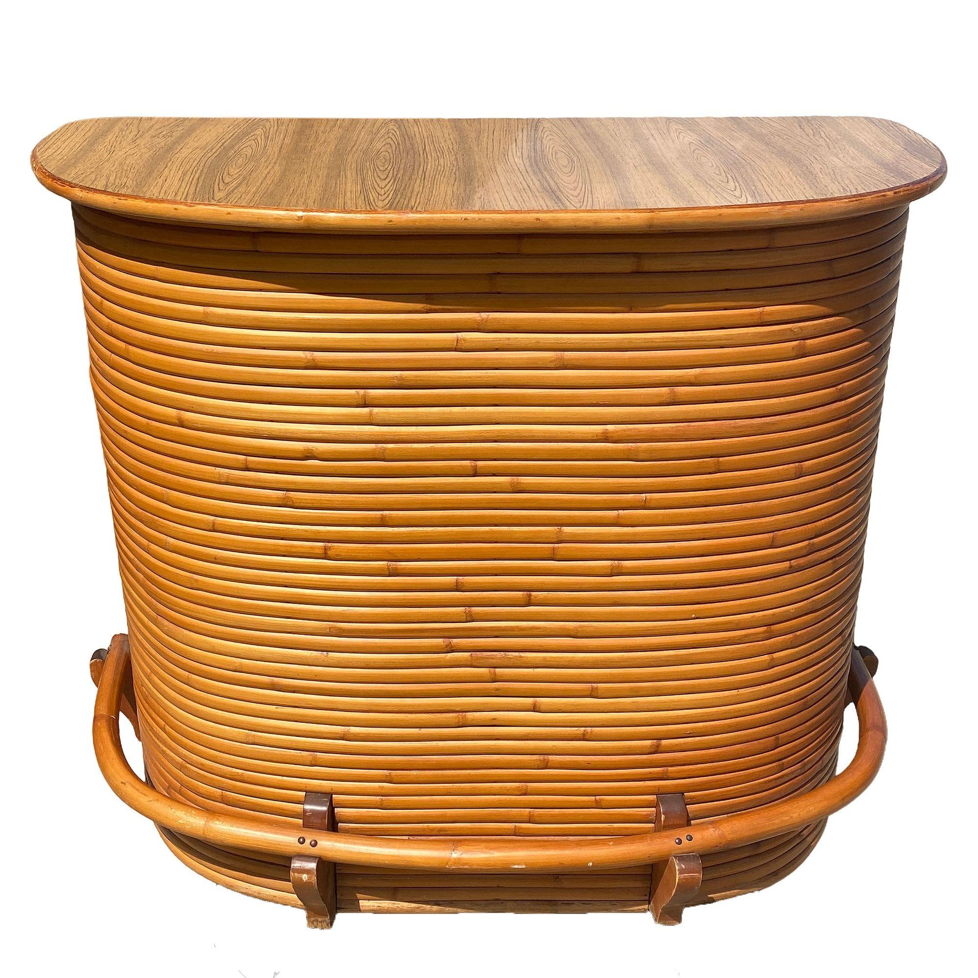 This beautifully restored Paul Frankl-inspired rattan bar features a sleek Formica top and root rest. This exquisite bar seamlessly blends Mid-century era styling with a Hawaiian flair. The front features vertically stacked rattan poles holding a