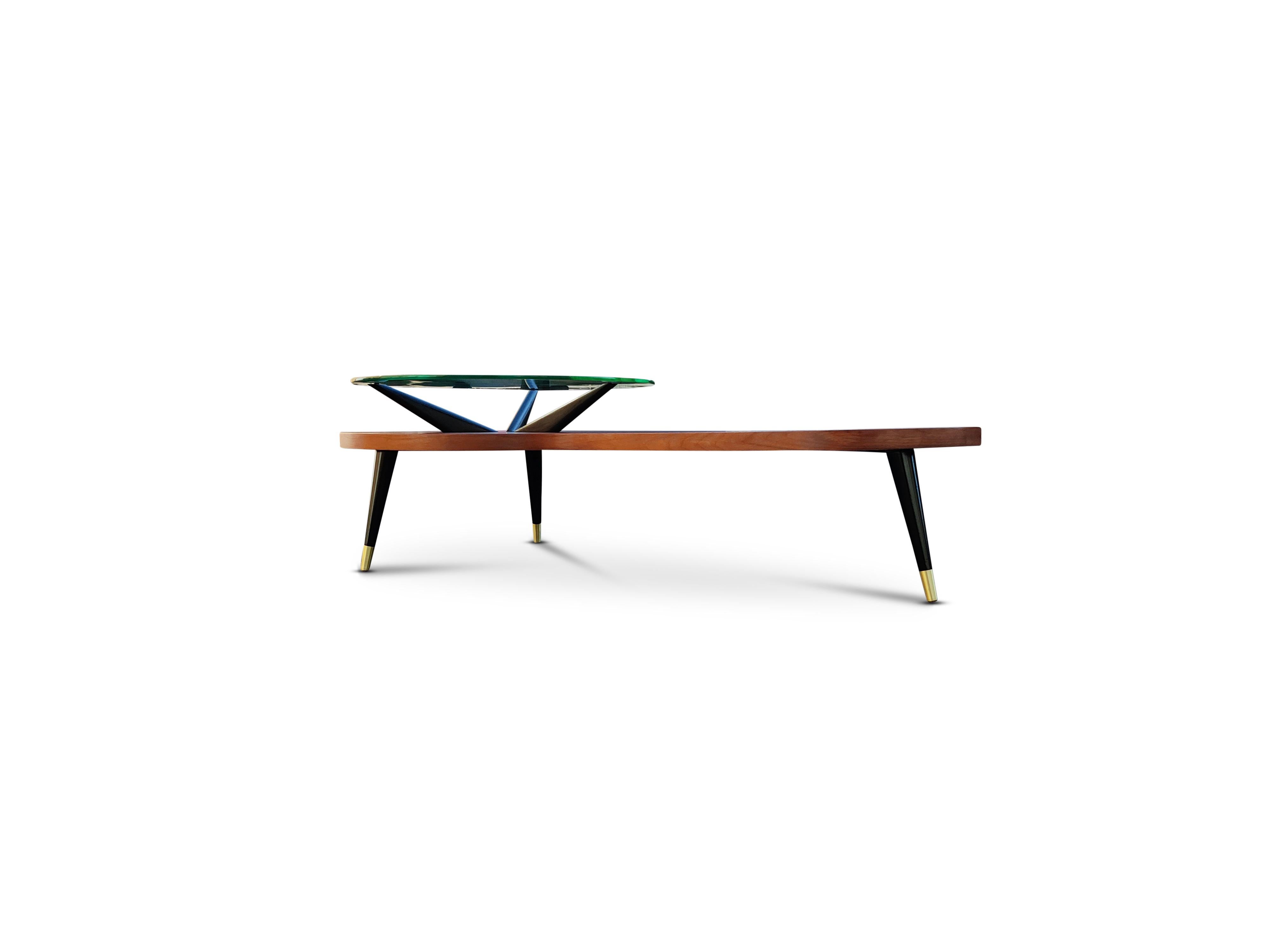 In the manner of Adrian Pearsall, a coffee table with three tapered walnut legs with brass caps, and a floating round glass top. Pearsall is known for his use of sculptural forms and bold organic lines. His designs often feature unique and