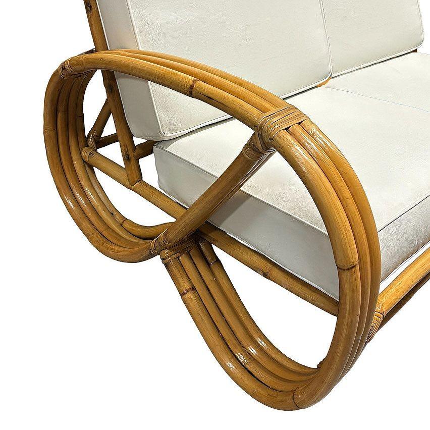 Questo divano componibile in rattan a 2 posti con braccio pretzel 3/4, splendidamente restaurato e ispirato a Paul Frankl, presenta il noto bracciolo pretzel 3/4 inverso su ciascuna estremità con un arco decorativo lungo la base. Il divano è