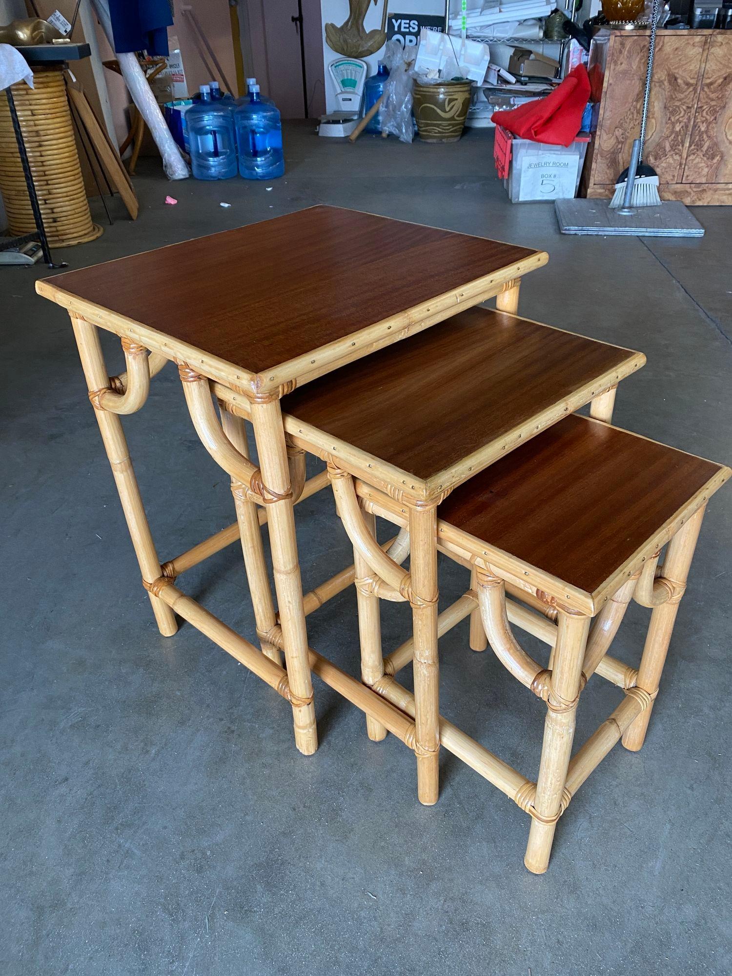 This beautifully restored set of 3 Frankl style Rattan nesting tables with inset mahogany tabletops. The Rattan used for these nesting tables was imported from the Philippines and assembled in the United States, as is typical of high-end Rattan of