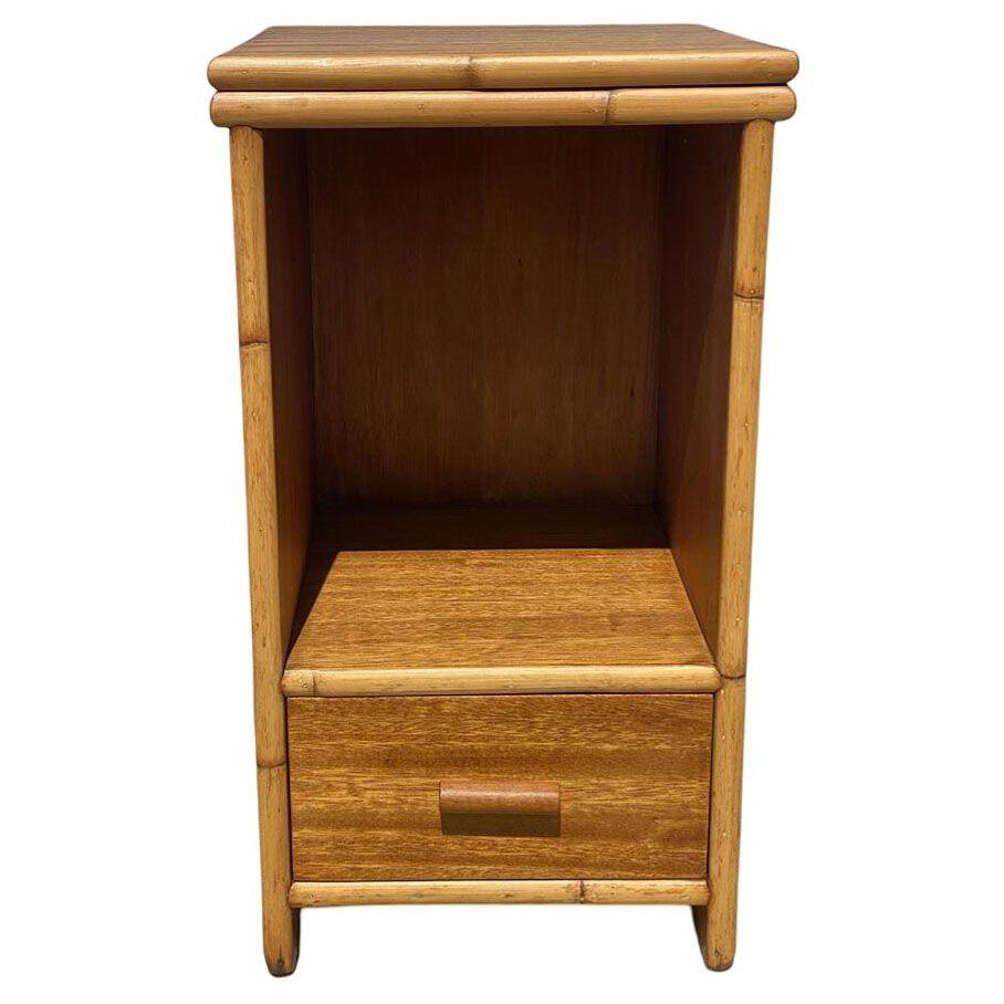This beautifully restored 1950s rattan and koa wood bedside table blends style with vintage charm, and modern comfort. the table features rattan trim and a single drawer. The table features a stacked rattan base with a drawer underneath, a large