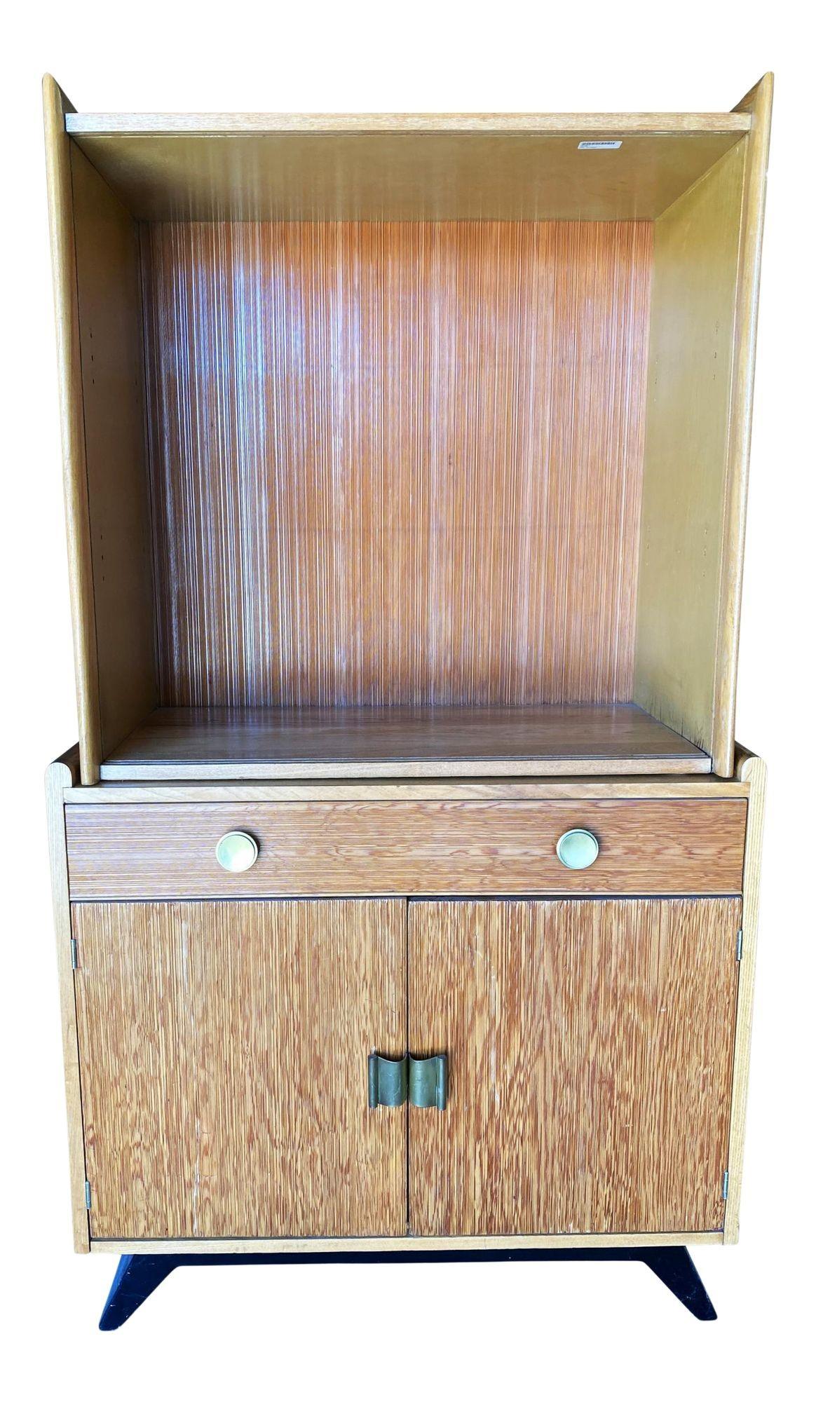 Original circa 1940 early midcentury display cabinet featuring 3 glass self/glass door cabinet which rests on a single drawer cabinet. This cabinet is Designed by Paul Frankl and features his trademark combed wood sides with curled brass pulls.