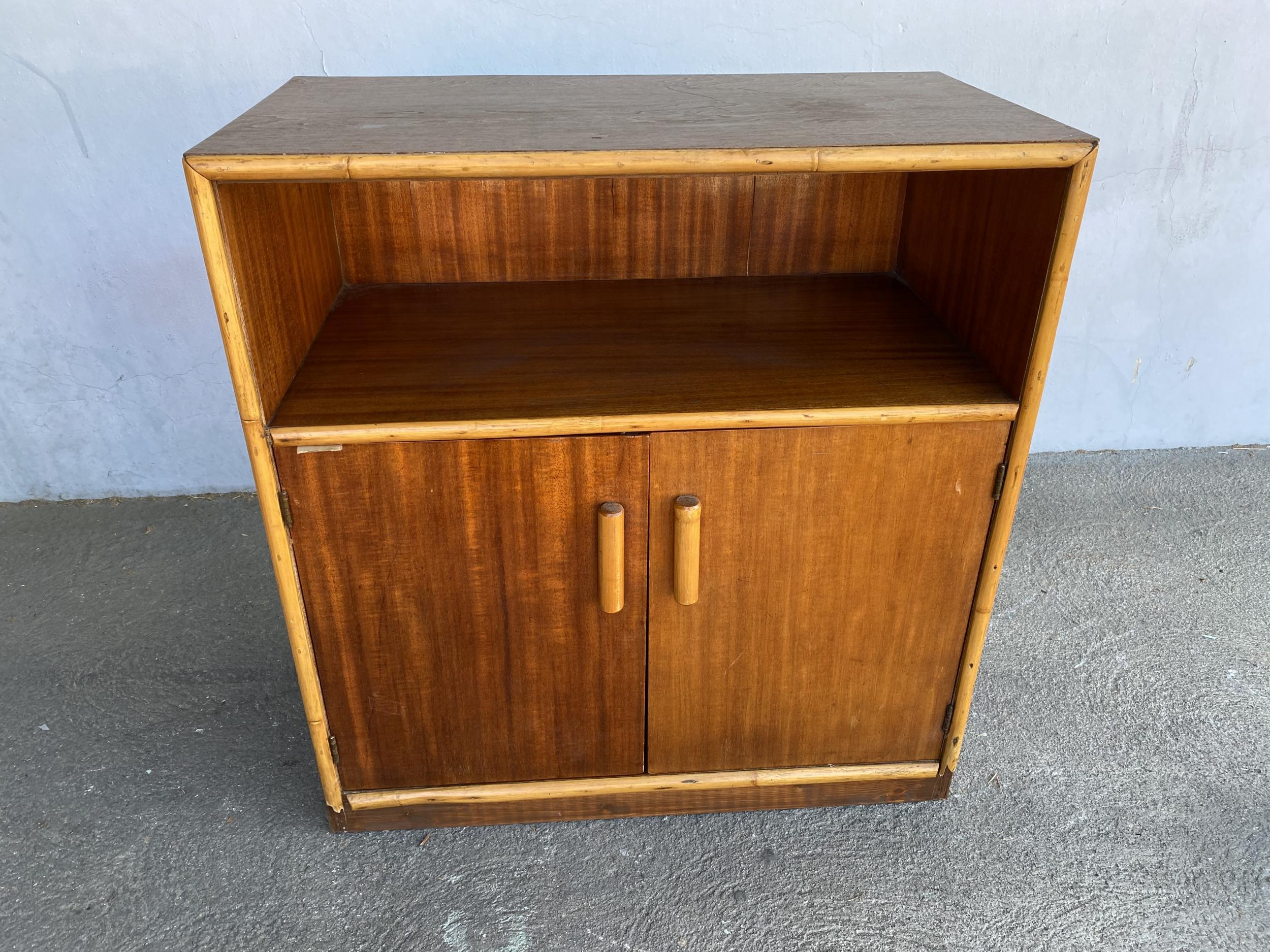 Restored Post War mahogany cabinet with rattan accents featuring a rattan trim with single shelf cubby space and a 2 door cabinet underneath which opens to two fixed shelves.

Restored to new for you.

All rattan, bamboo, and wicker furniture