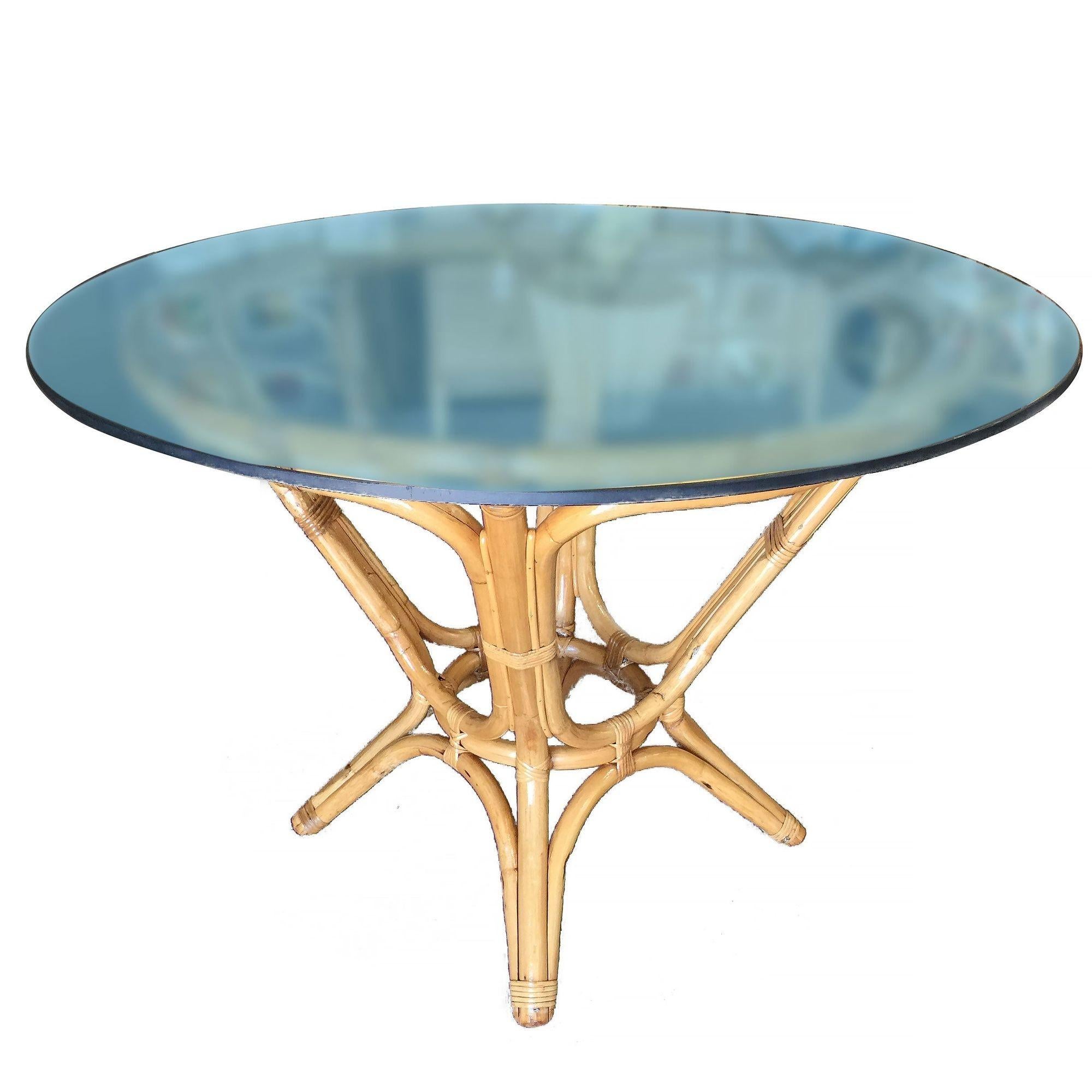 Elegant midcentury dining table features a sculptural hourglass rattan base with a round glass top. The table can easily accommodate four guests depending on the choice of chairs. Restored to new for you. All rattan, bamboo and wicker furniture has