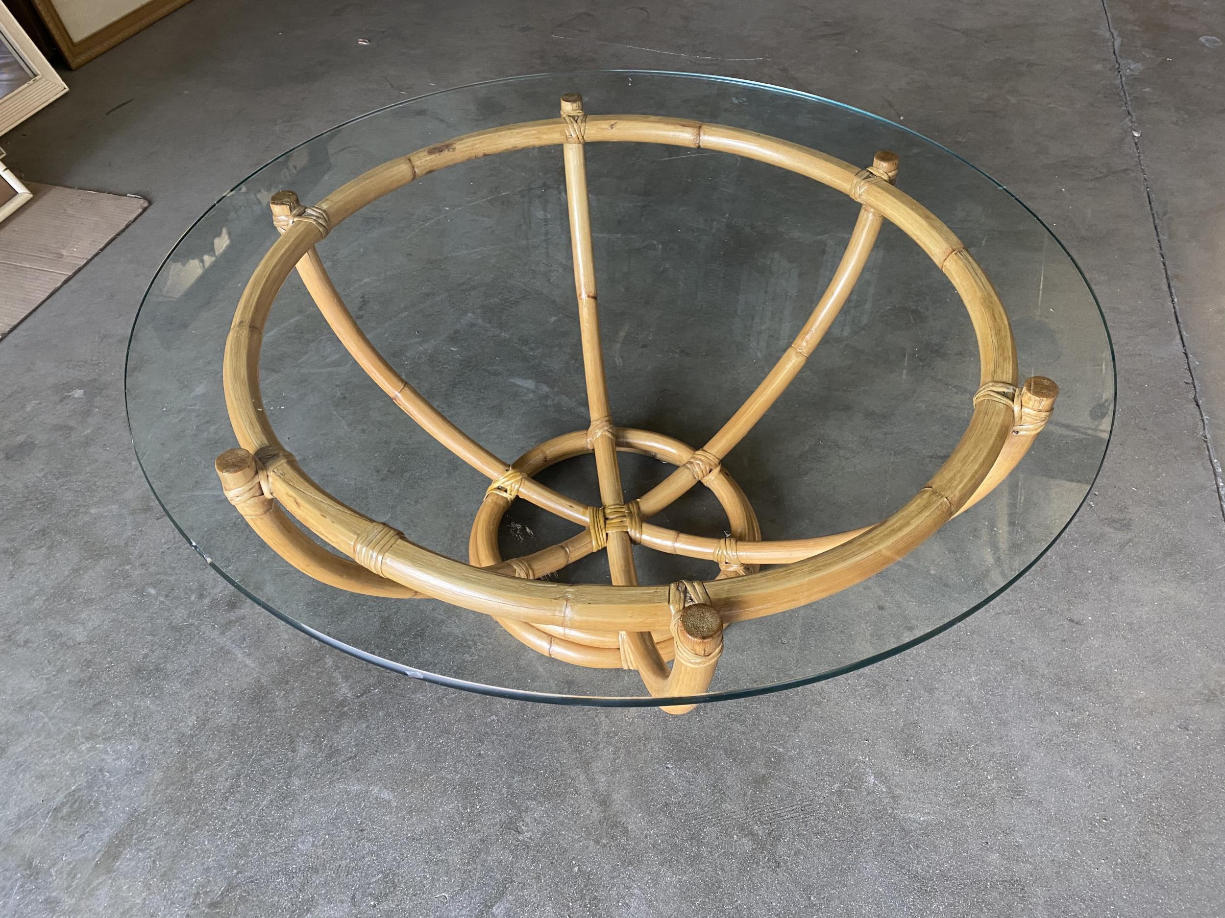 Made circa 1940, this six-pole rattan coffee table has an unusual stacked rattan round base. The six rattan poles organically branch outward to a circular top made of a single piece of bent rattan. The glass top rests atop the poles, exuding an