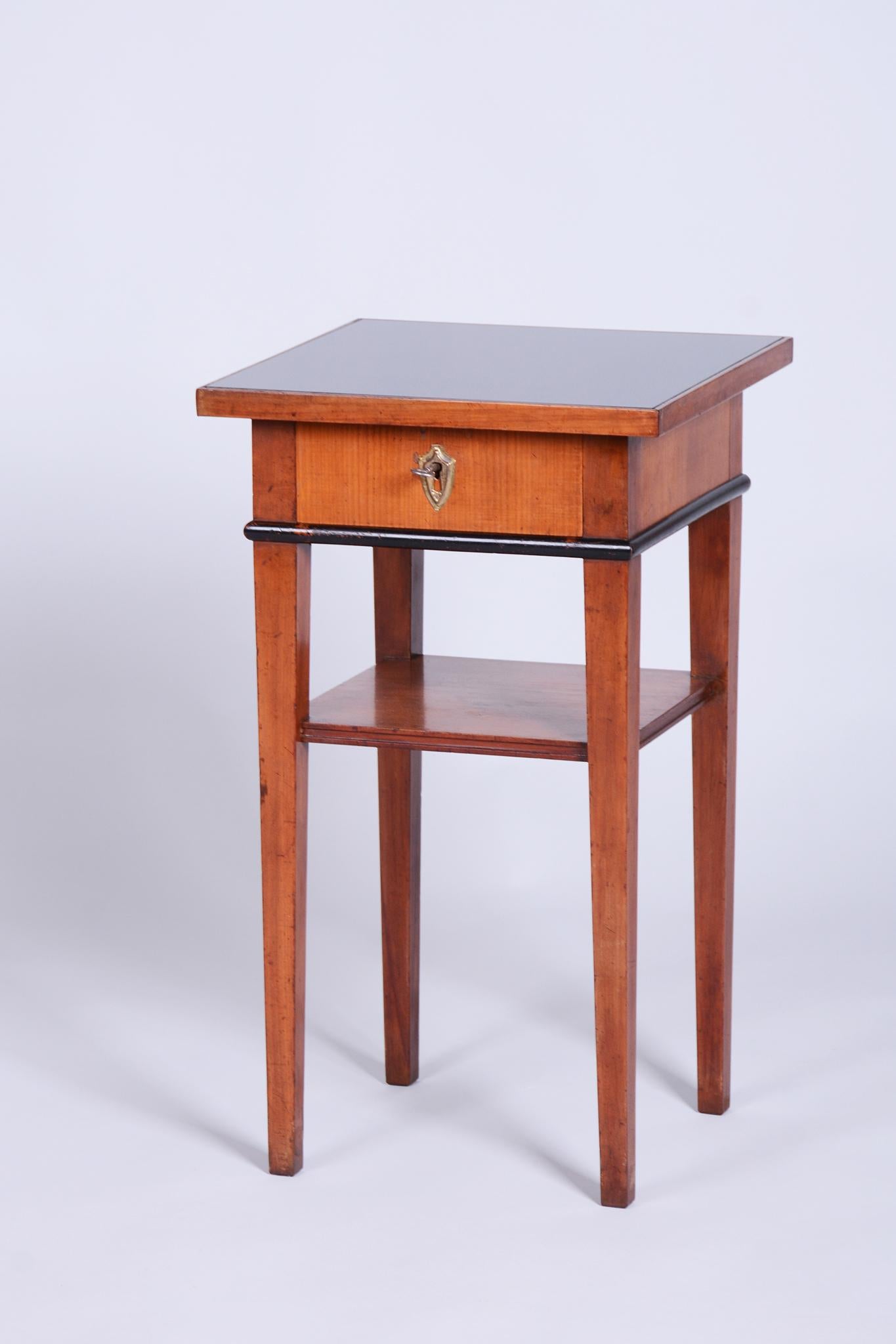Questo elegante tavolo Biedermeier proviene dalla Bohemia della metà del XIX secolo. È realizzato in legno massiccio e impiallacciato di ciliegio e ha un piano in vetro nero. Il tavolo è stato sottoposto a un accurato restauro, durante il quale sono