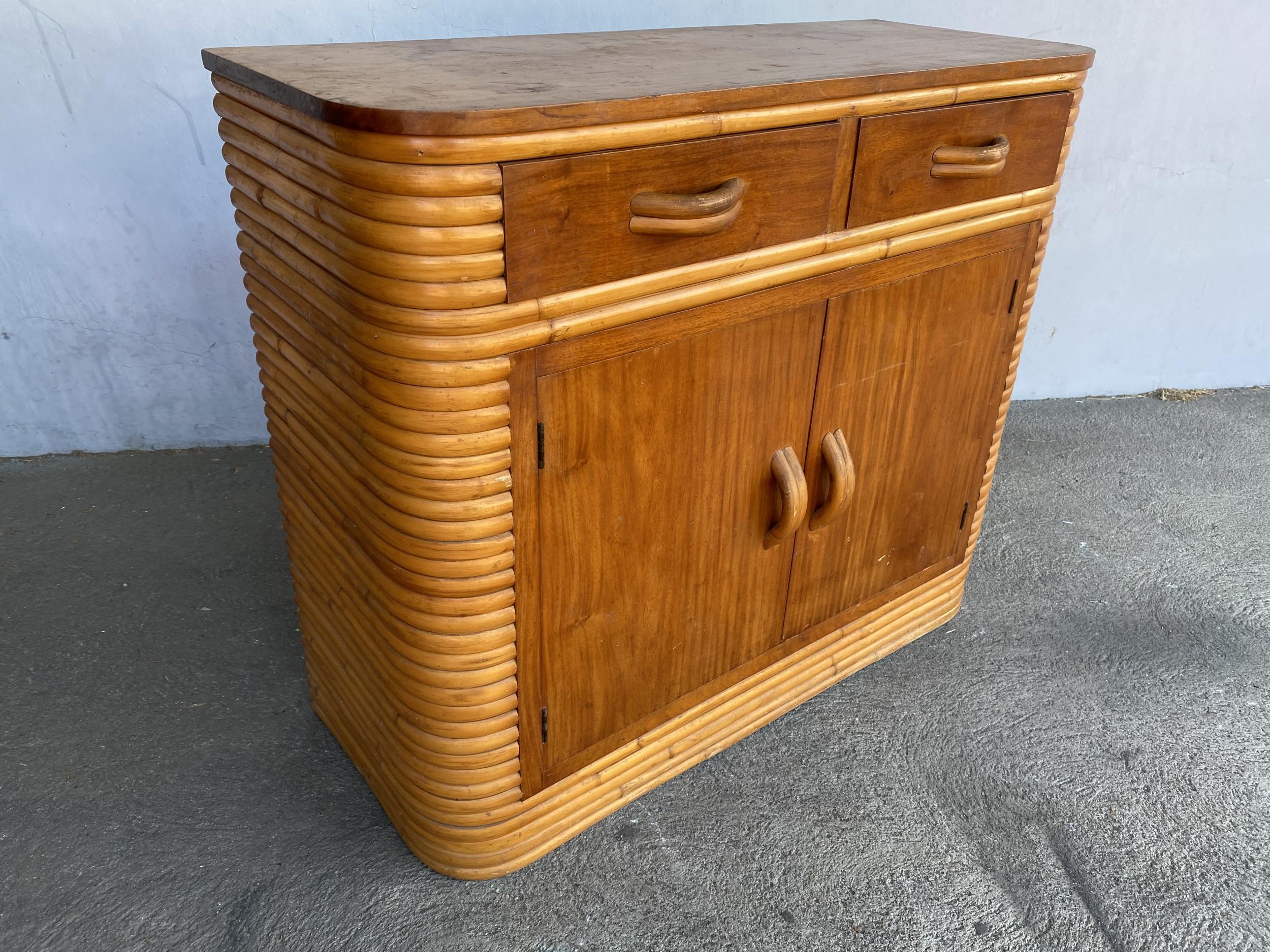 Stacked rattan cabinet with a mahogany top and two pull-out drawers and two-door cabinet underneath, circa 1940.

Restored to new for you.

All rattan, bamboo, and wicker furniture has been painstakingly refurbished to the highest standards with