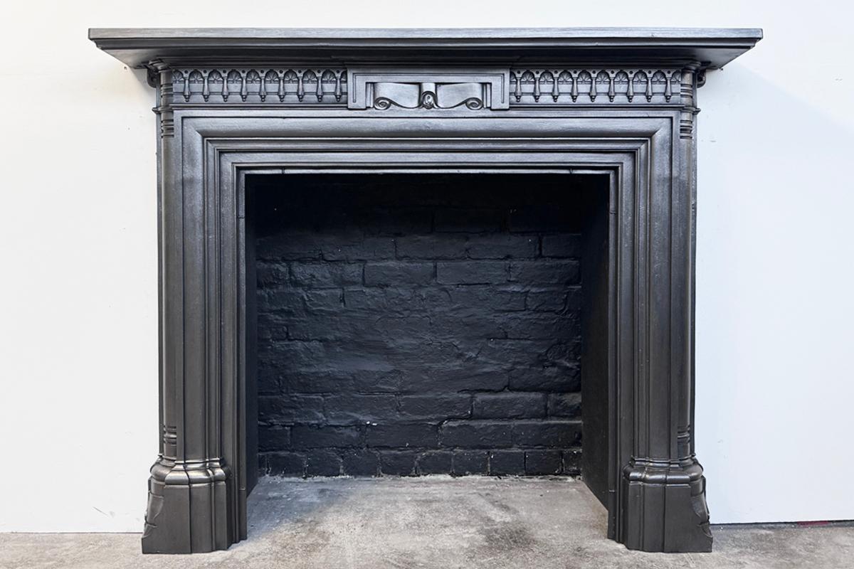 A restored Victorian cast iron fireplace surround. Complex moulded plinths support deep legs with quarter-rounded outside returns. Alternating tassels and fans across the frieze centred by ribbon scroll. The whole is sitting below a generous shelf. 