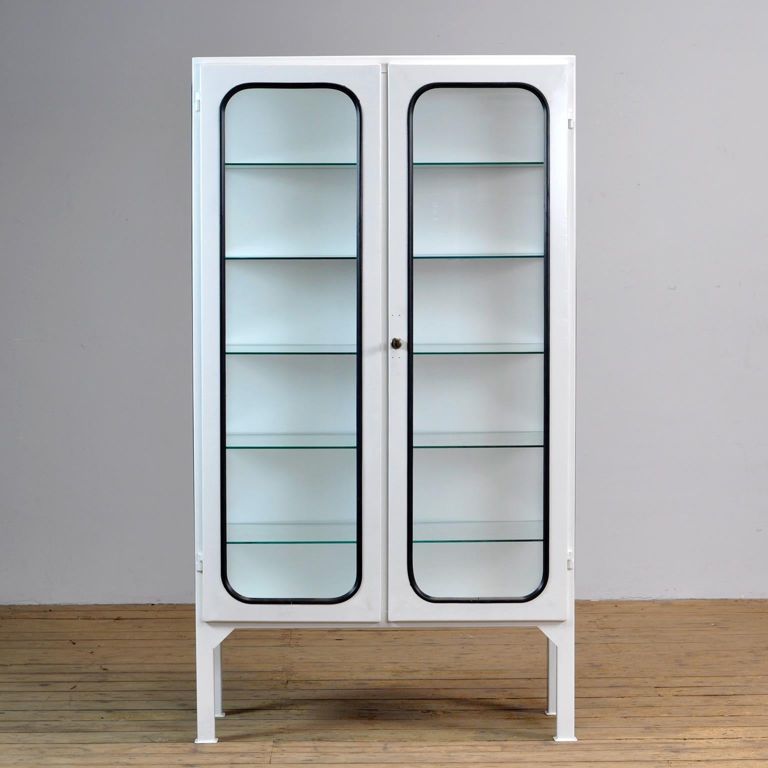 This medicine cabinet was designed in the 1970s and was produced circa 1975 in Hungary. It is made from iron and antique glass, and the glass is held by a black rubber strip. The cabinet features five adjustable glass shelves and a functioning
