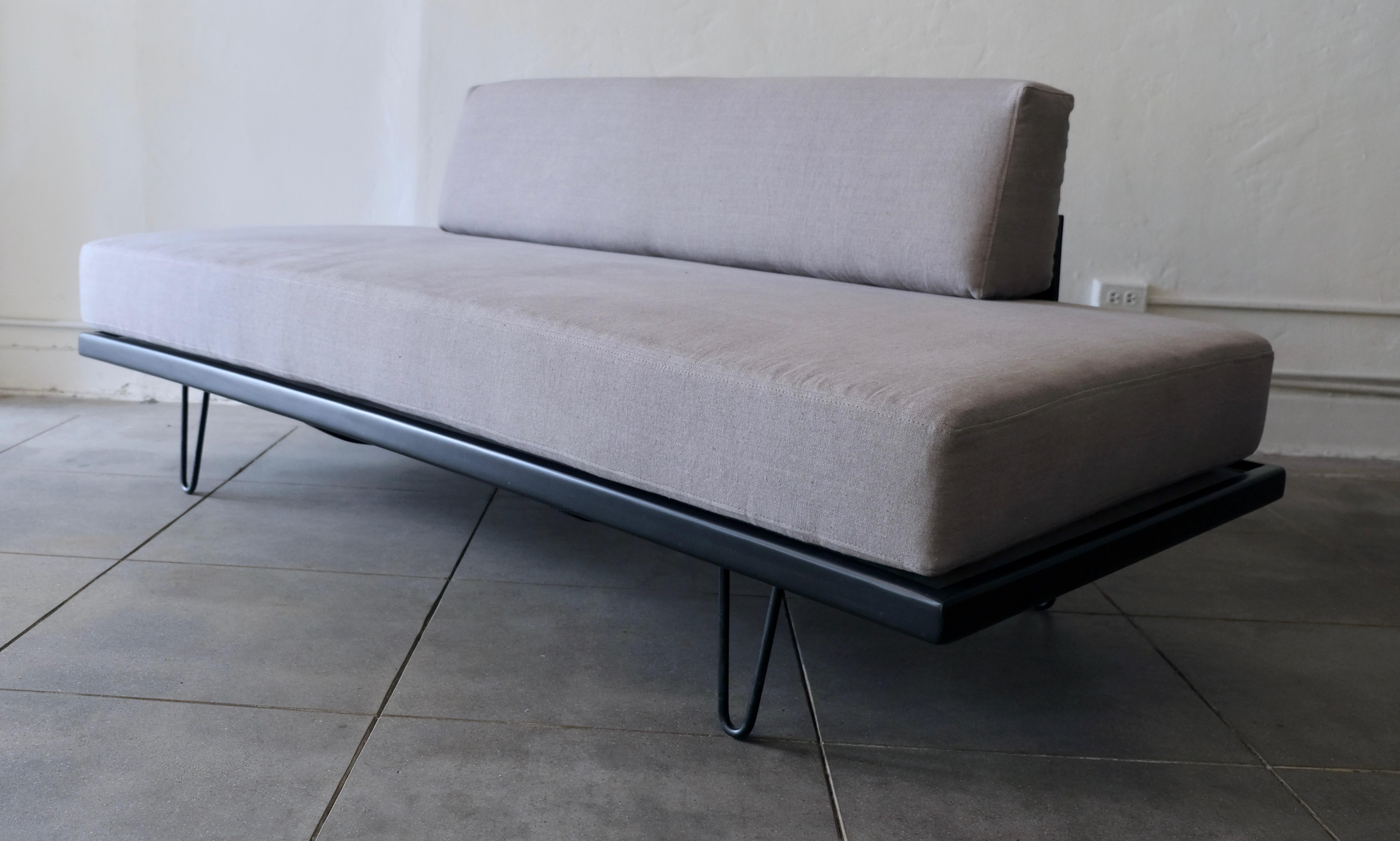 A vintage daybed with clean Classic Mid-Century Modern lines. The daybed is supported by four black metal V-shaped legs. The piece has been refinished and reupholstered with a gray linen fabric.
  