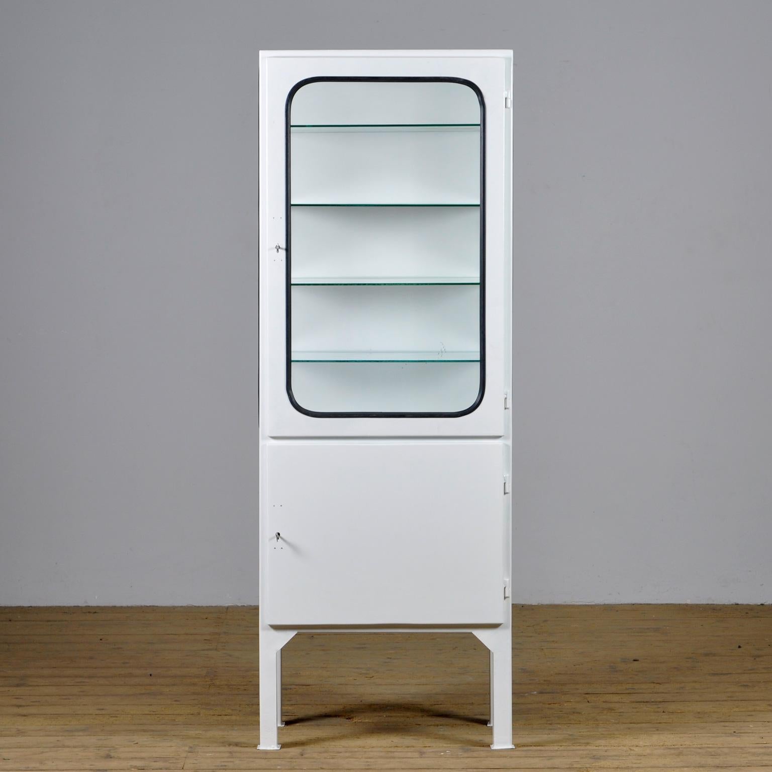 This medical cabinet was designed in the 1970s and was produced circa 1975 in hungary. It is made from iron and glass with new glass shelves. The glass is held by a black rubber strip. The cabinet features two adjustable glass shelves and a
