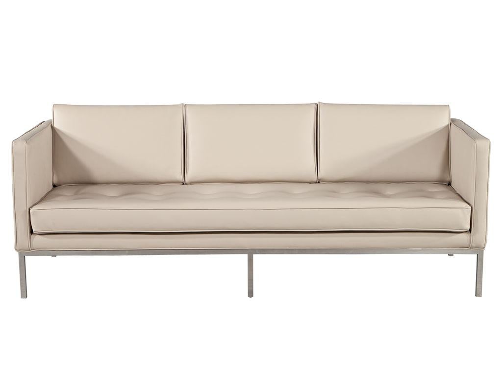 Restored Vintage Mid-Century Modern Tufted Sofa in Cream Faux Leather. America circa 1970’s, this mid-century modern classic has been restored to its original glory. Featuring beautiful cream faux leather with loose cushions and tufted seat