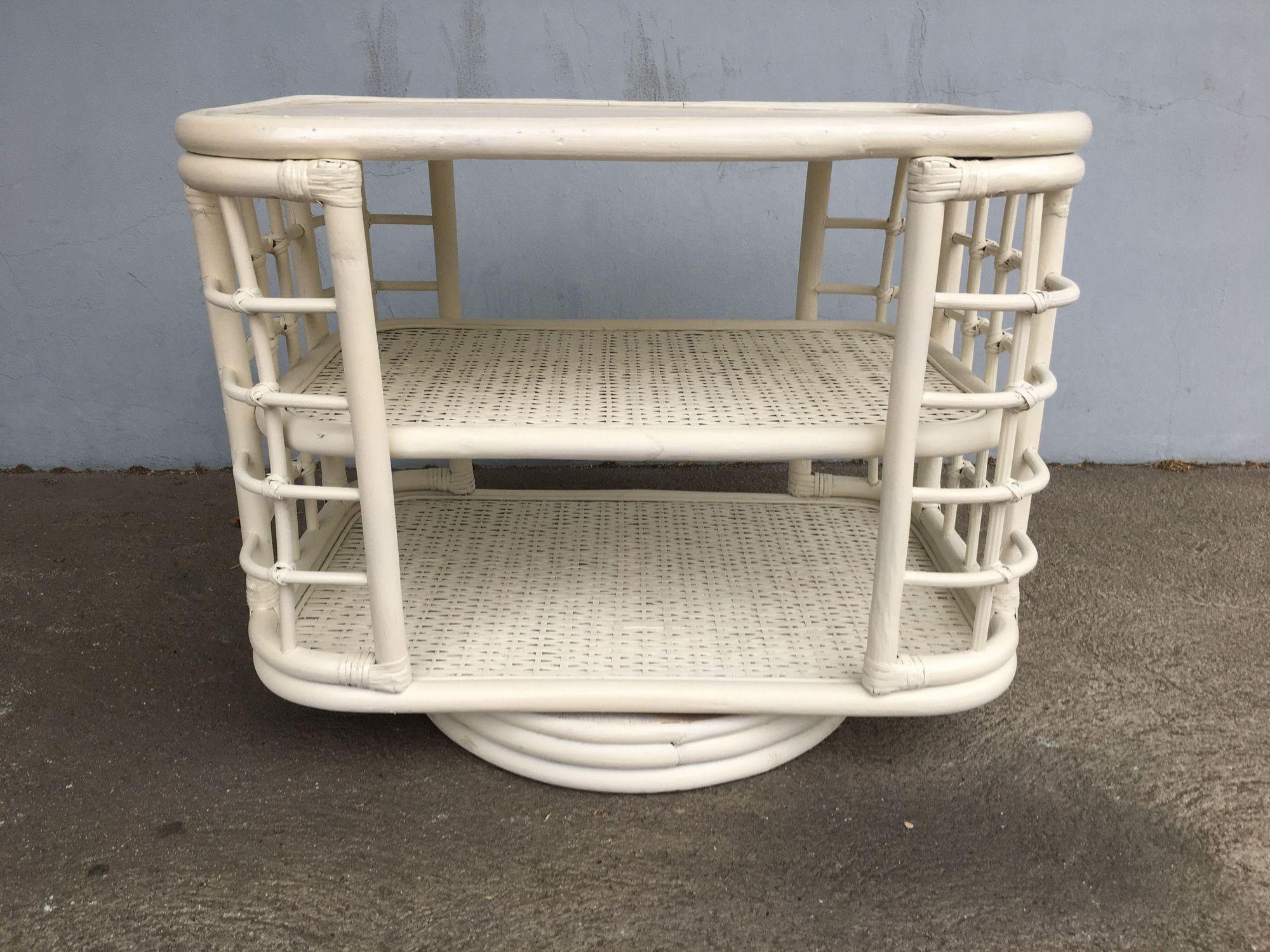 White Painted Mid Century era rattan side table bookshelf featuring two shelves with skeleton side walls and a swivel base for easy book location.

1970, United States

We only purchase and sell only the best and finest rattan furniture made by