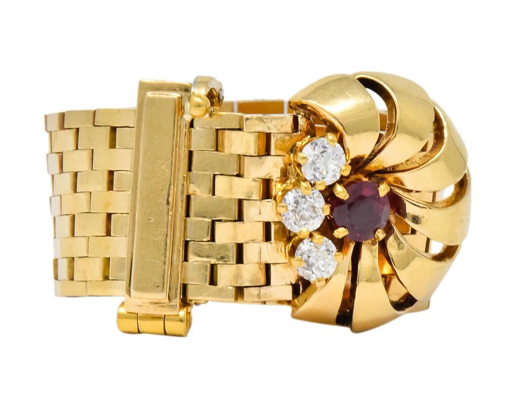 Designed as mesh linked buckle ring with pierced stylized flower motif

Centering, a prong set, round cut ruby weighing approximately 0.21 carat, transparent and a medium-dark very slightly purplish-red

With three prong set transitional cut
