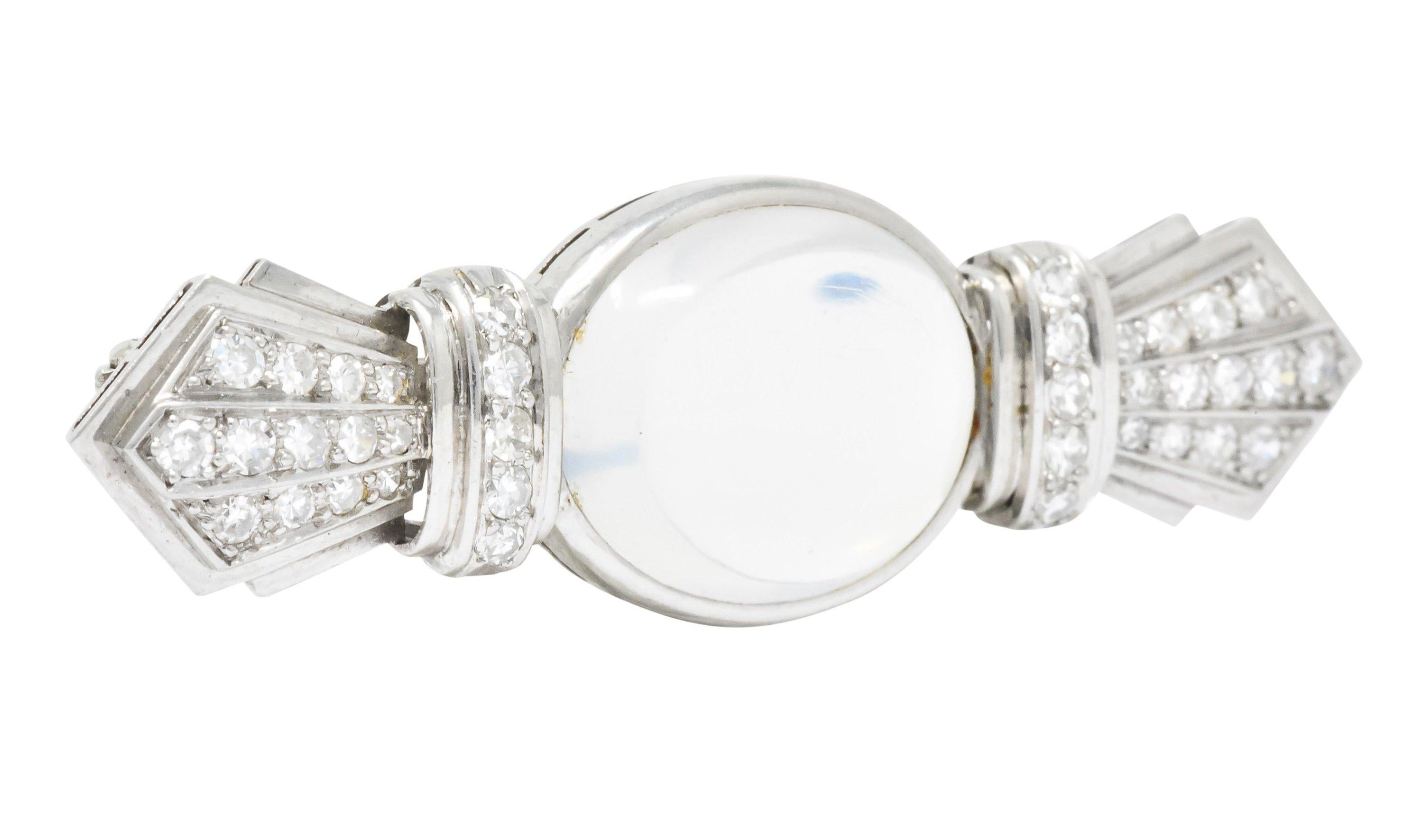 Bar style brooch centering an oval moonstone cabochon measuring 5/8 x 1/2 inch, transparent with moderate blue adularescence

Flanked by two pointed deco forms, accented throughout by rows of single cut diamonds weighing approximately 0.70 carat,
