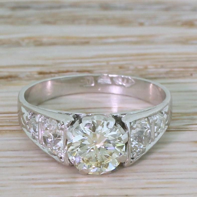 A bold and impressive vintage engagement ring. The round brilliant cut diamond in the centre displays the softest, subtle champagne hue – the colour of which is emphasised by the high white diamonds in the shoulders. The centre stone is secured in