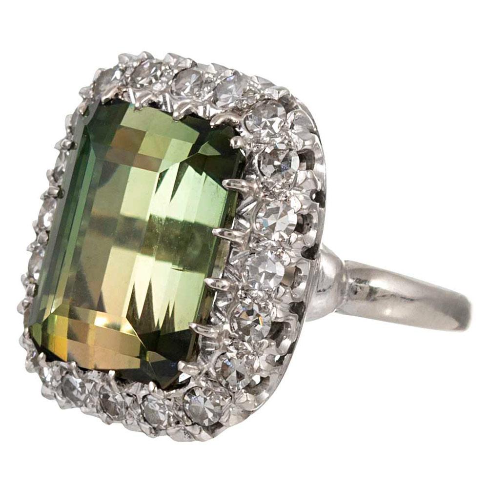 A classic cluster centered upon a 12 carat rectangular green tourmaline framed by twenty white diamonds that weigh approximately 1 carat in total, the ring is rendered in 14 karat white gold. Note the beautiful under-gallery. This neutral hue looks