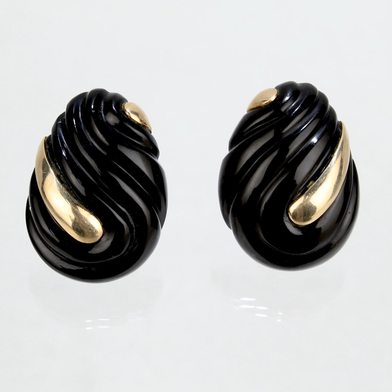 A cool pair of carved onyx and gold earrings.

Comprised of tear-drop shaped carved onyx inlaid with gold accents.

With omega clip backs for extra security when wearing.

Marked to one post 14k for gold fineness.

A fun, cool retro pair of very