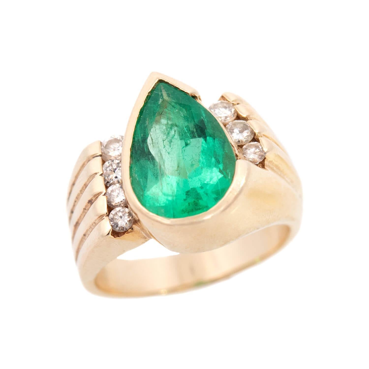 A gorgeous emerald and diamond ring from the Retro (ca1960s) era! Crafted in 14k yellow gold, the ring features a central pear cut emerald. The emerald is held within a bezel setting and has a carat weight of 4ct. The emerald is bordered on the