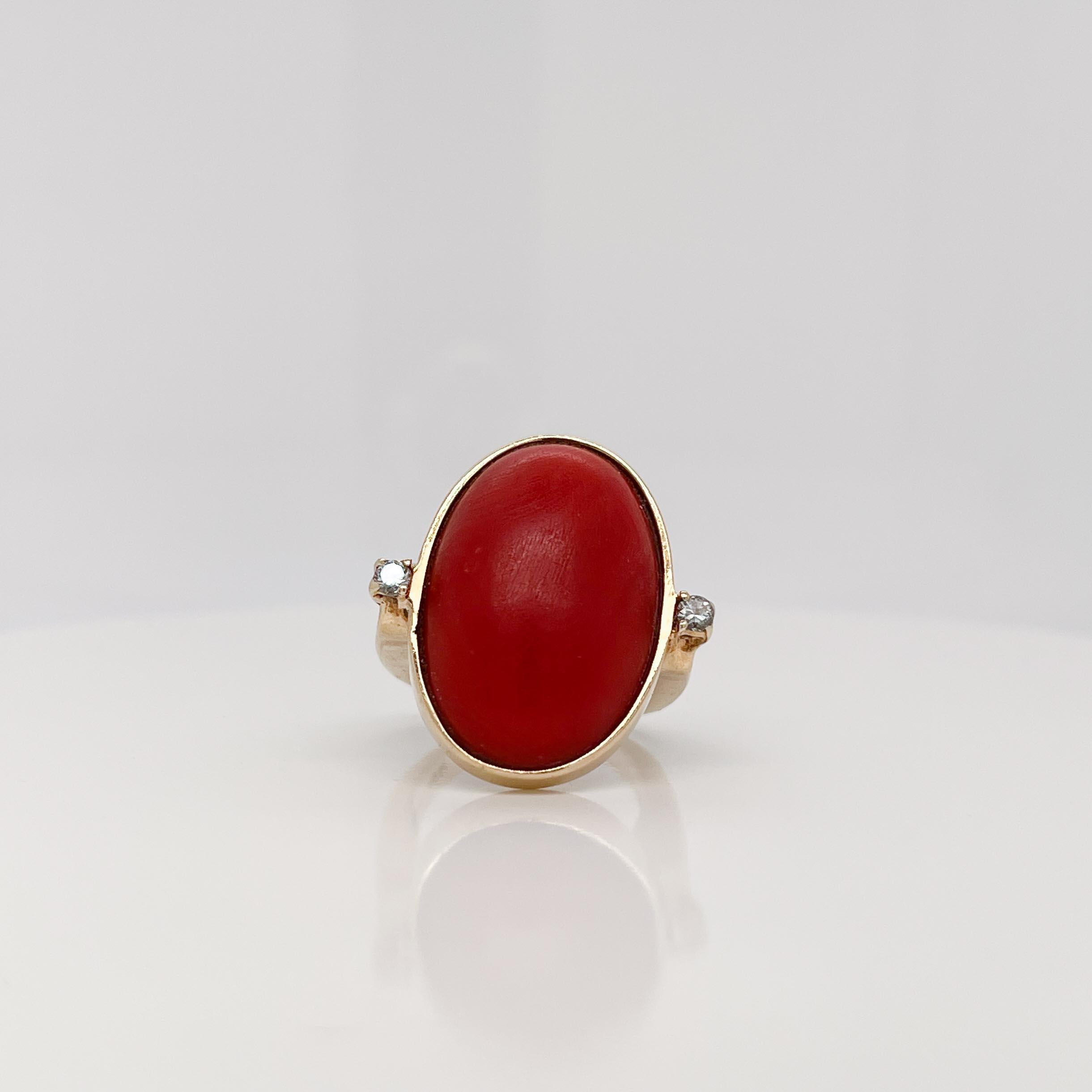 A fine Retro gold and coral signet ring.

With a large coral cabochon at the center of 14k gold setting that is flanked by two prong set round brilliant diamonds. 

The square band has open work on both sides.

Simply a great Retro signet-style